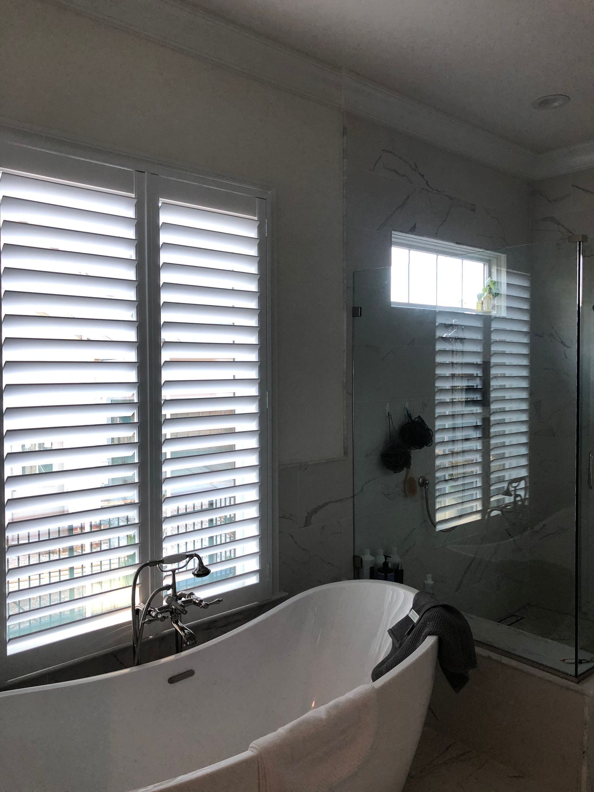 Bathroom with white shutters, a bathtub, and a window reflecting the shutters.