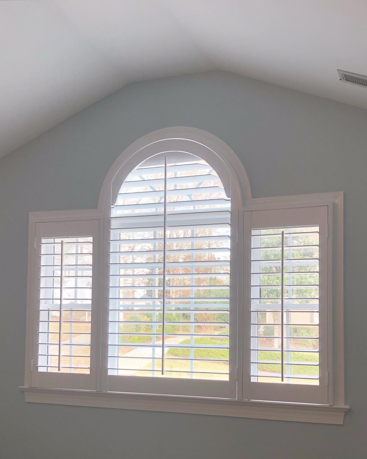 White shutters on arched window in light blue room.