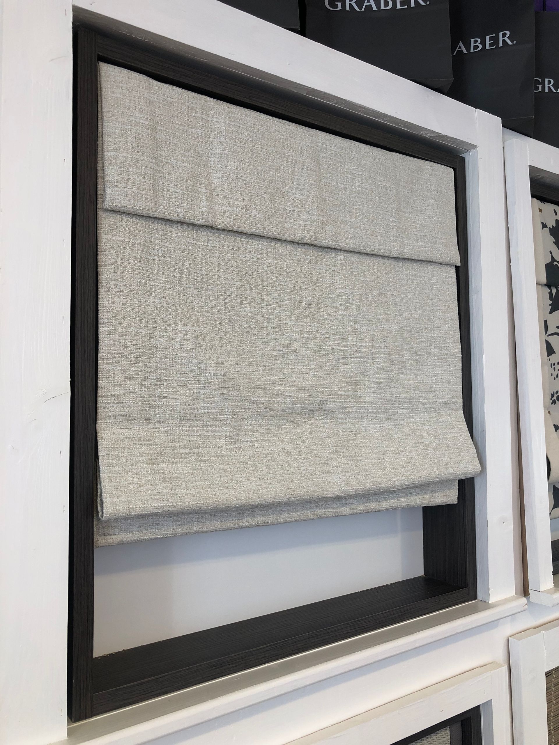 Gray fabric Roman shade displayed in a black-framed window.