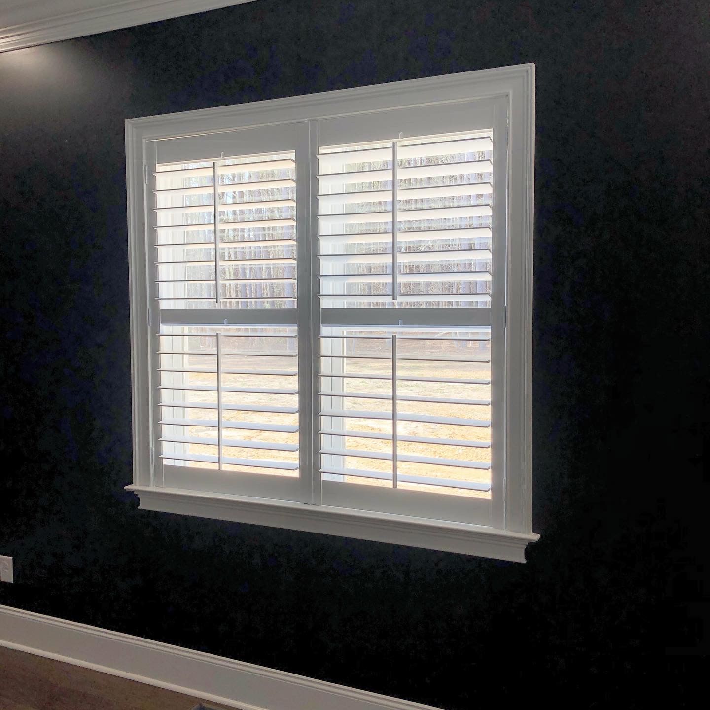 White shuttered window in white frame on black wall.