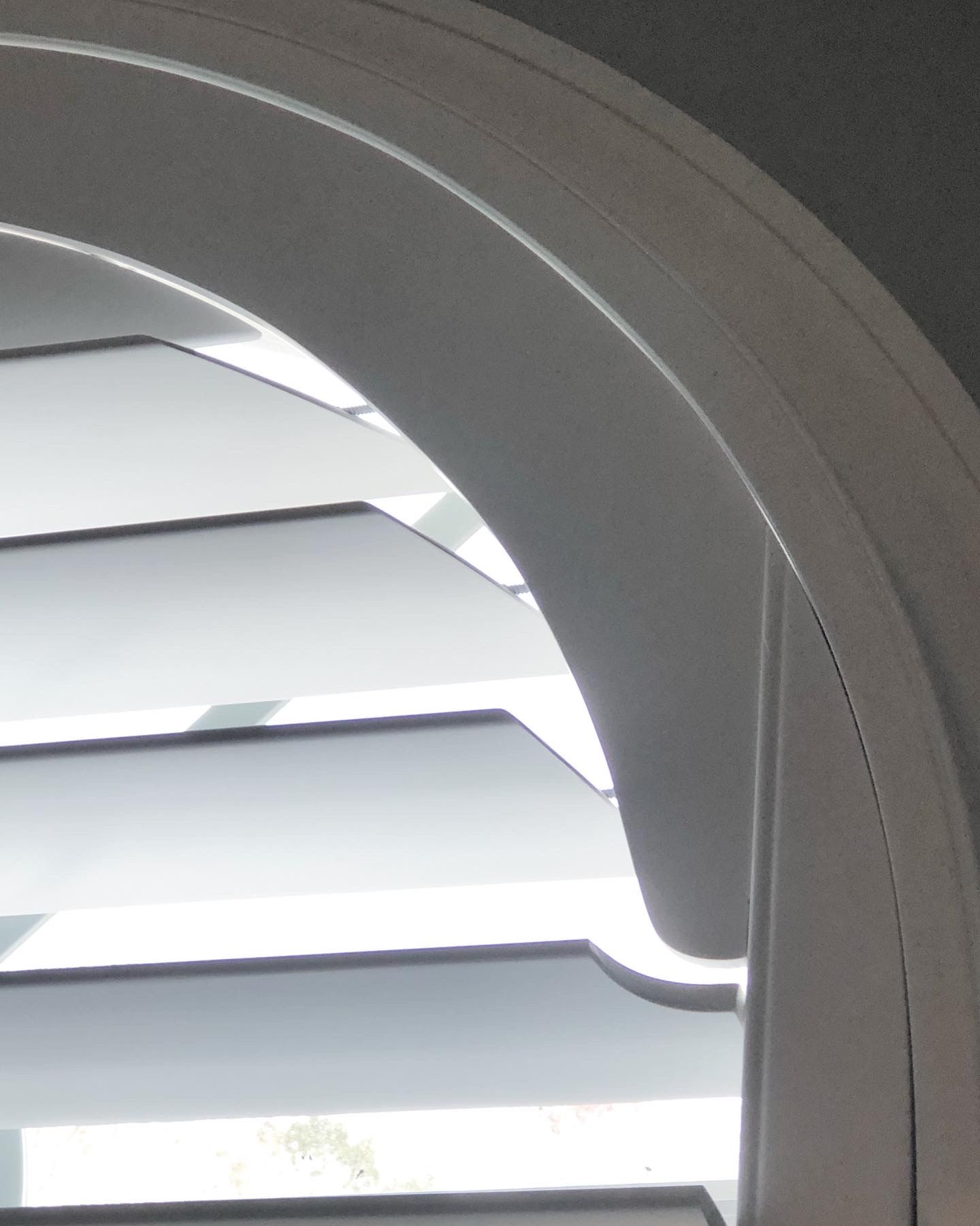 Close-up of white arched window shutters with angled slats.