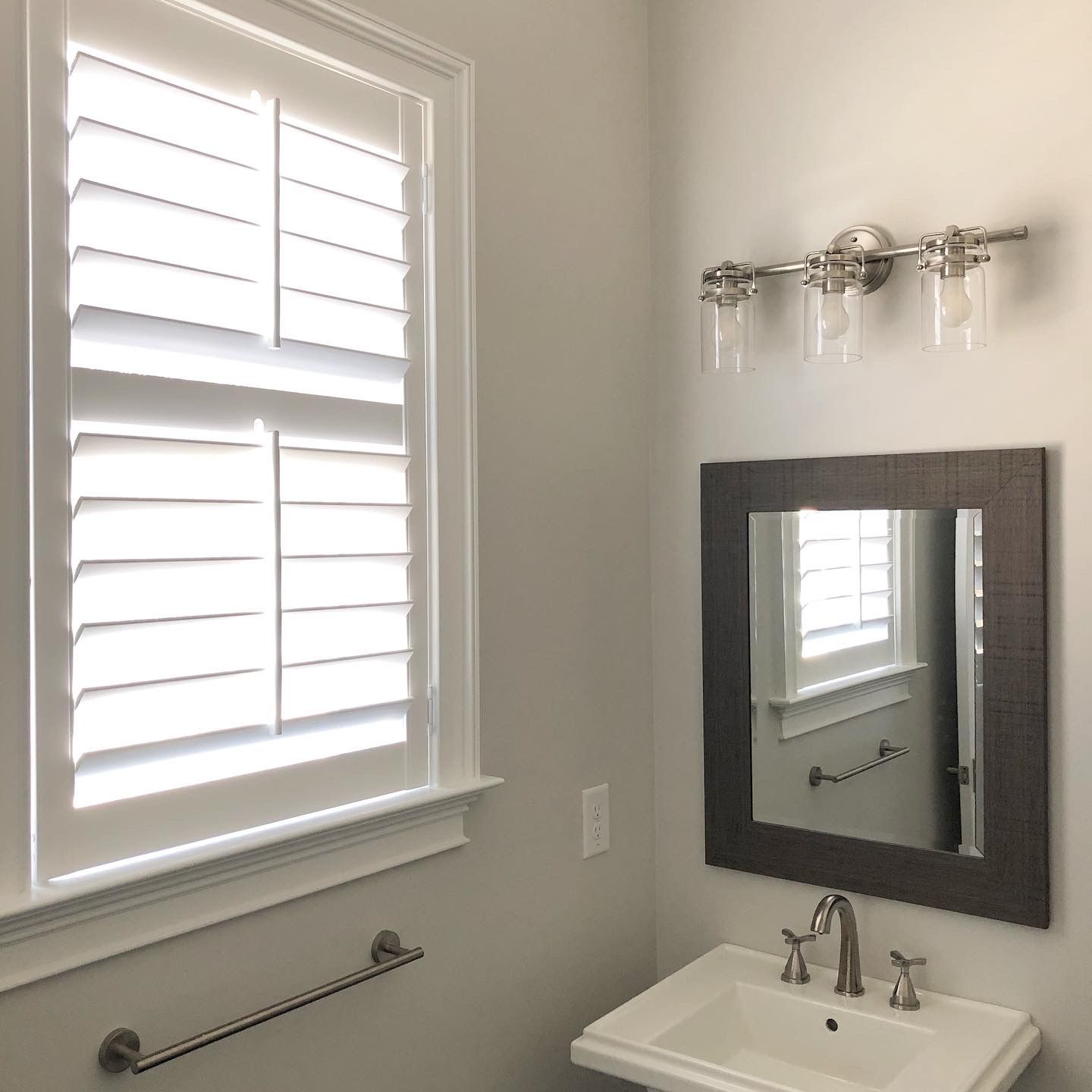 Bathroom with white shutters, light fixture above a mirror, and a sink.
