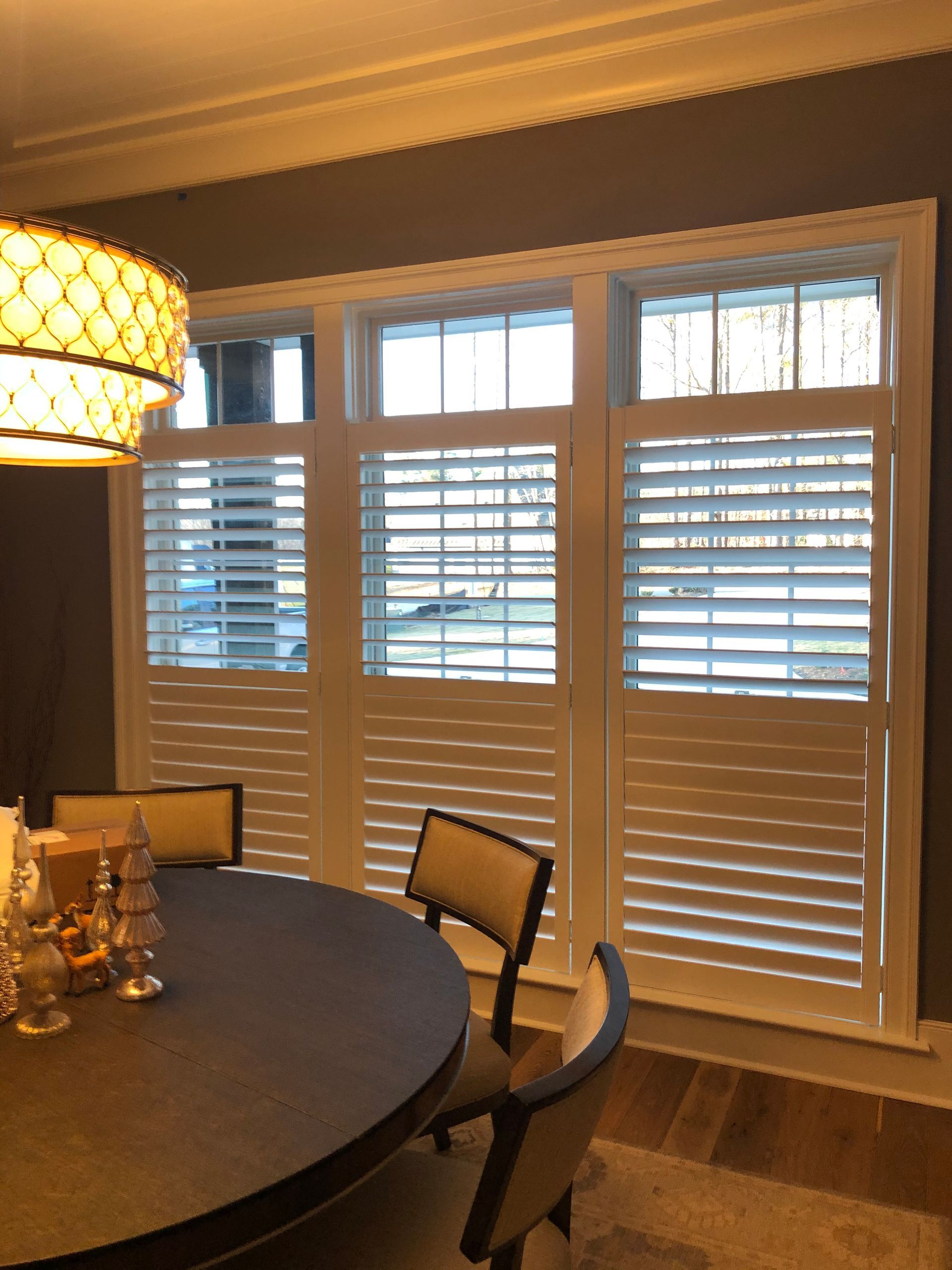 Dining room with white shuttered windows and round table.