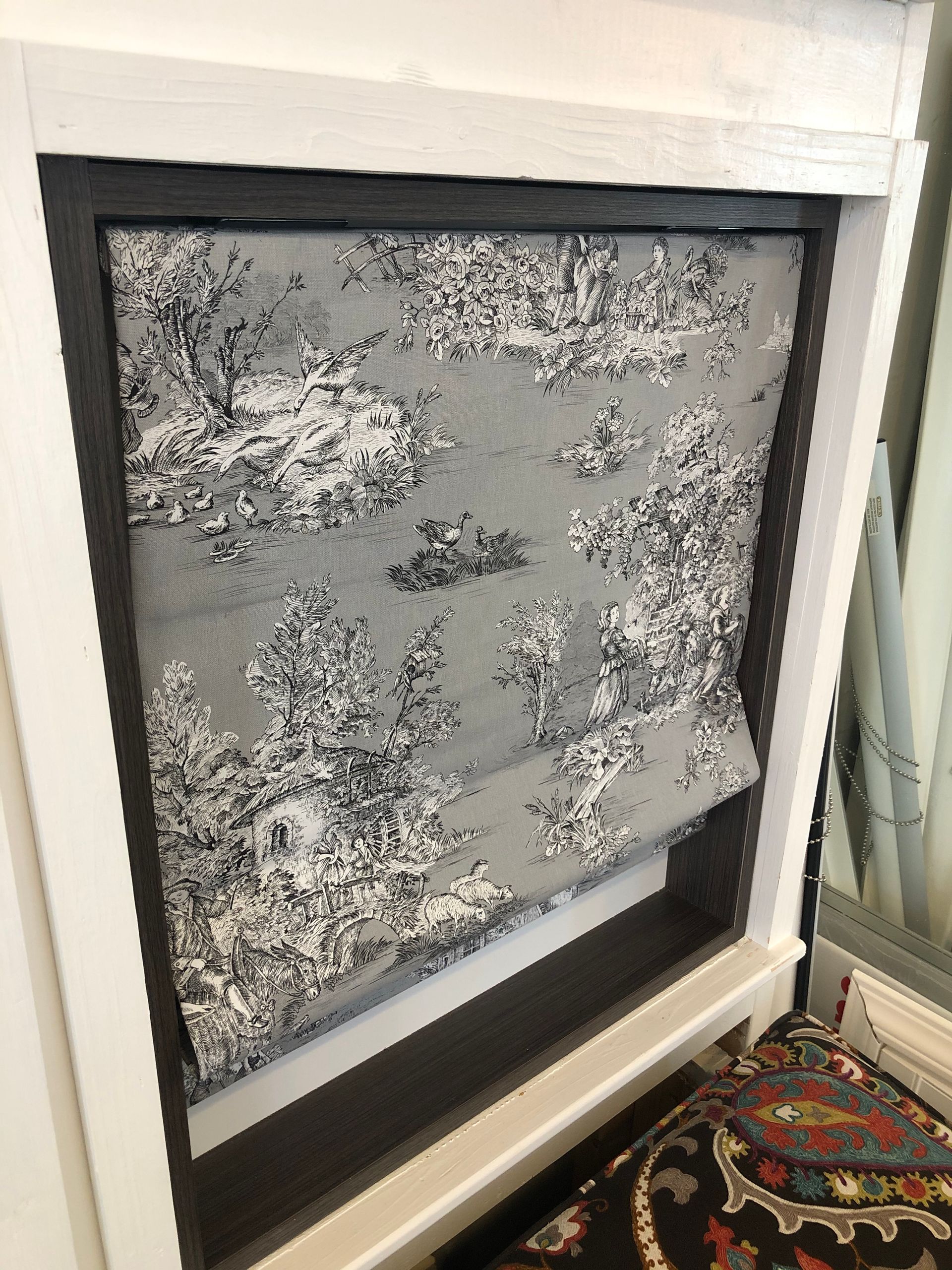 Gray toile fabric Roman shade inside a white framed window.
