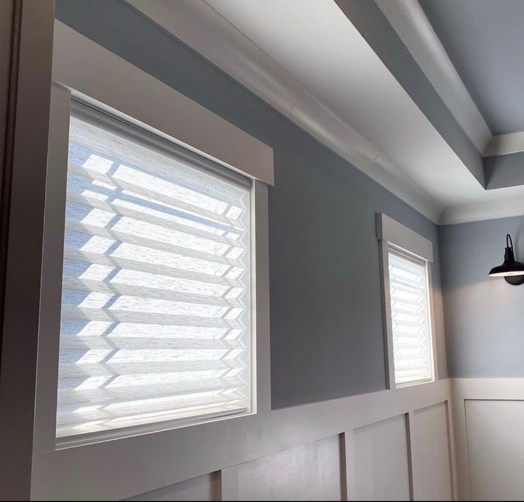 Two windows with white shades, blue walls, white trim and ceiling beams.