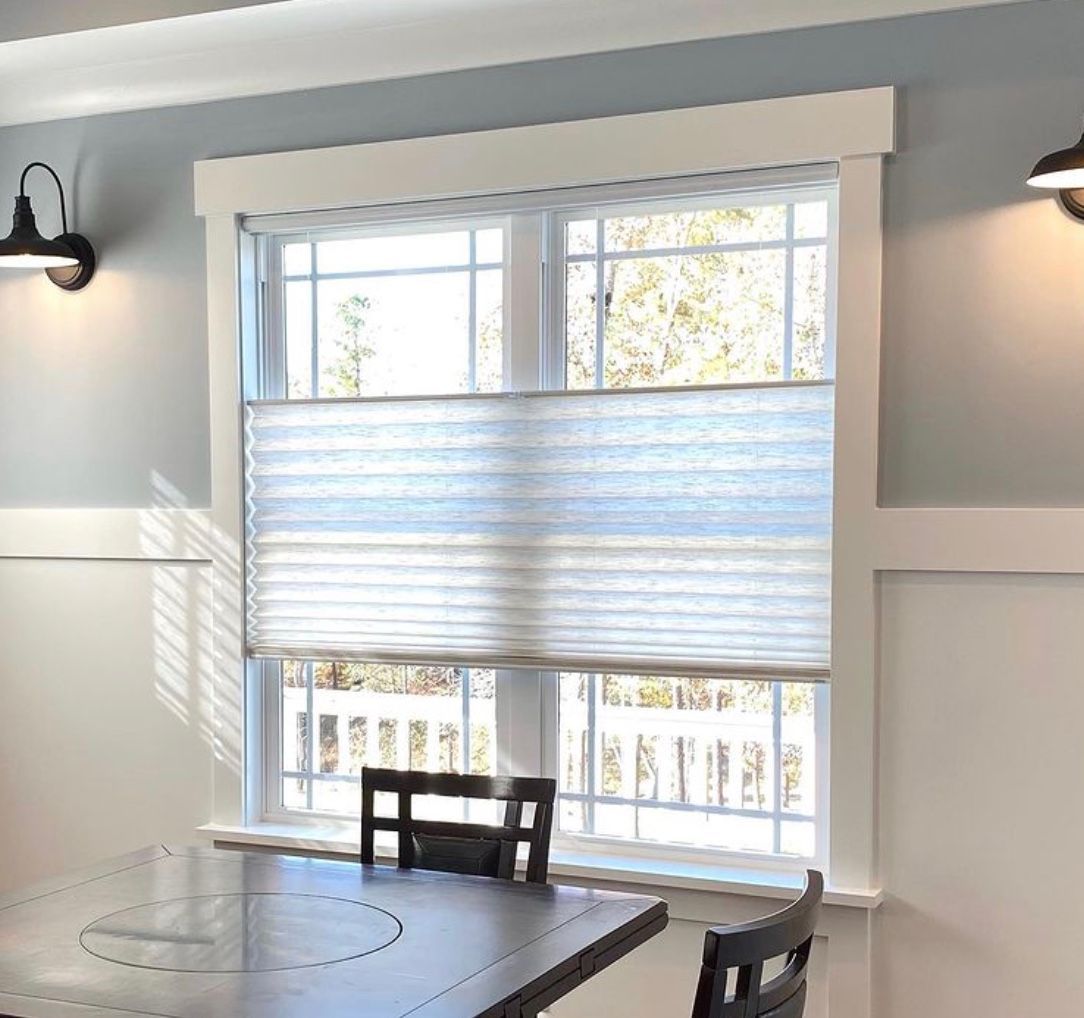 A window with light blue blinds, framed by white trim, over a dining table with chairs.