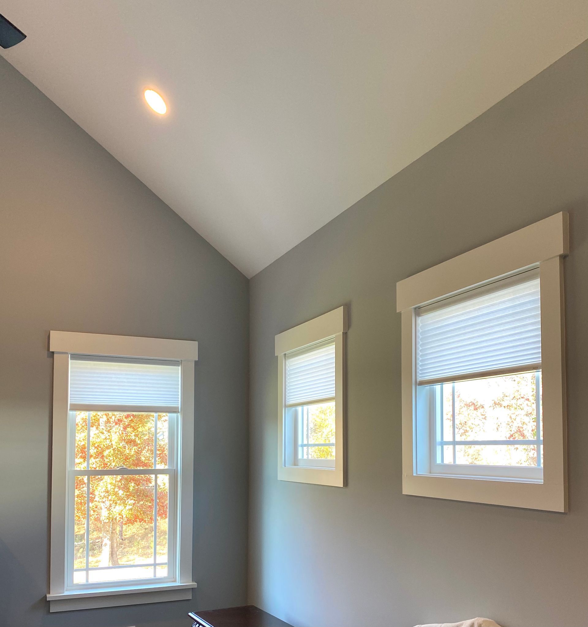 Interior corner with three windows, gray walls, white trim, and a high ceiling.