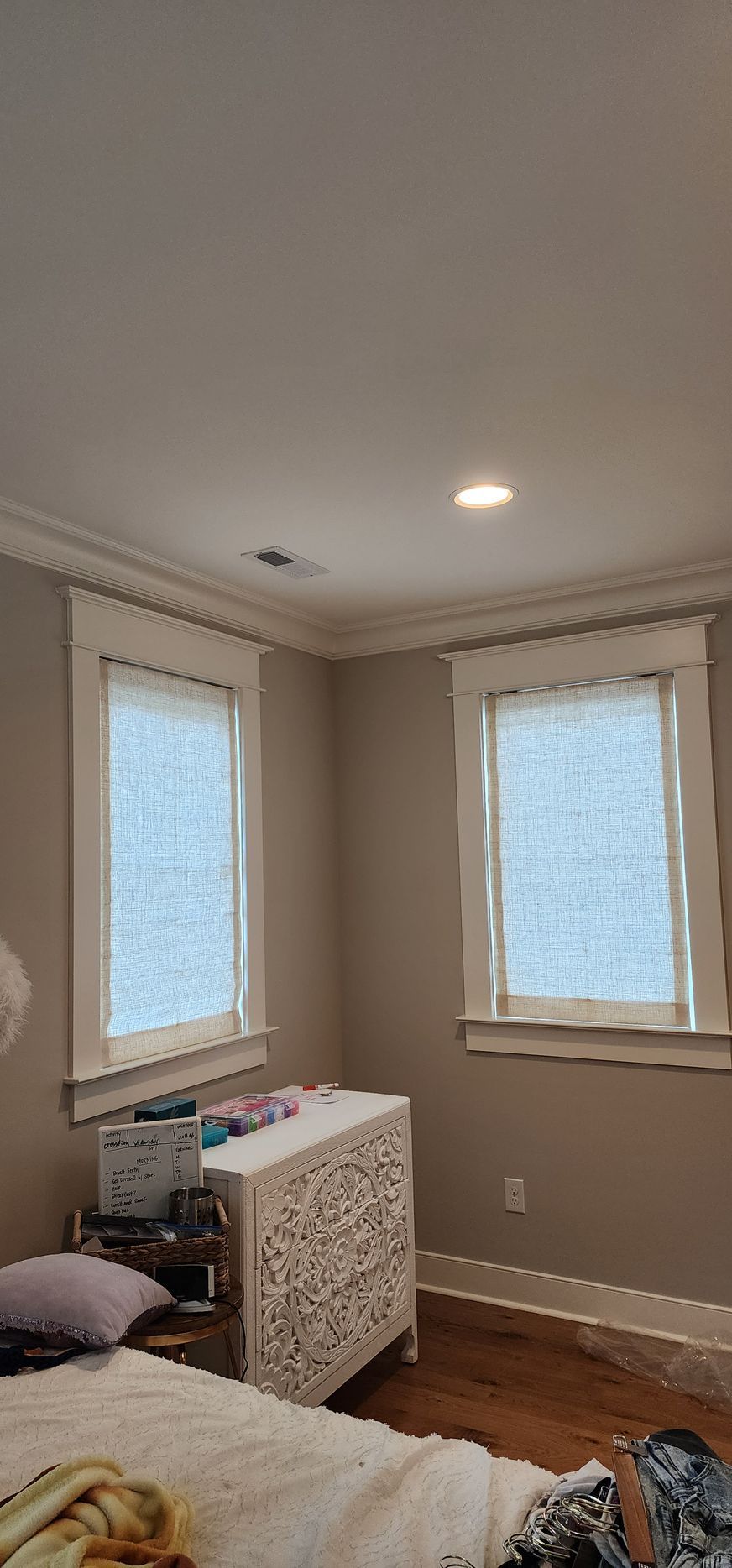 Bedroom corner with two windows, a white dresser, and part of a bed. Light tan walls, white trim and ceiling.