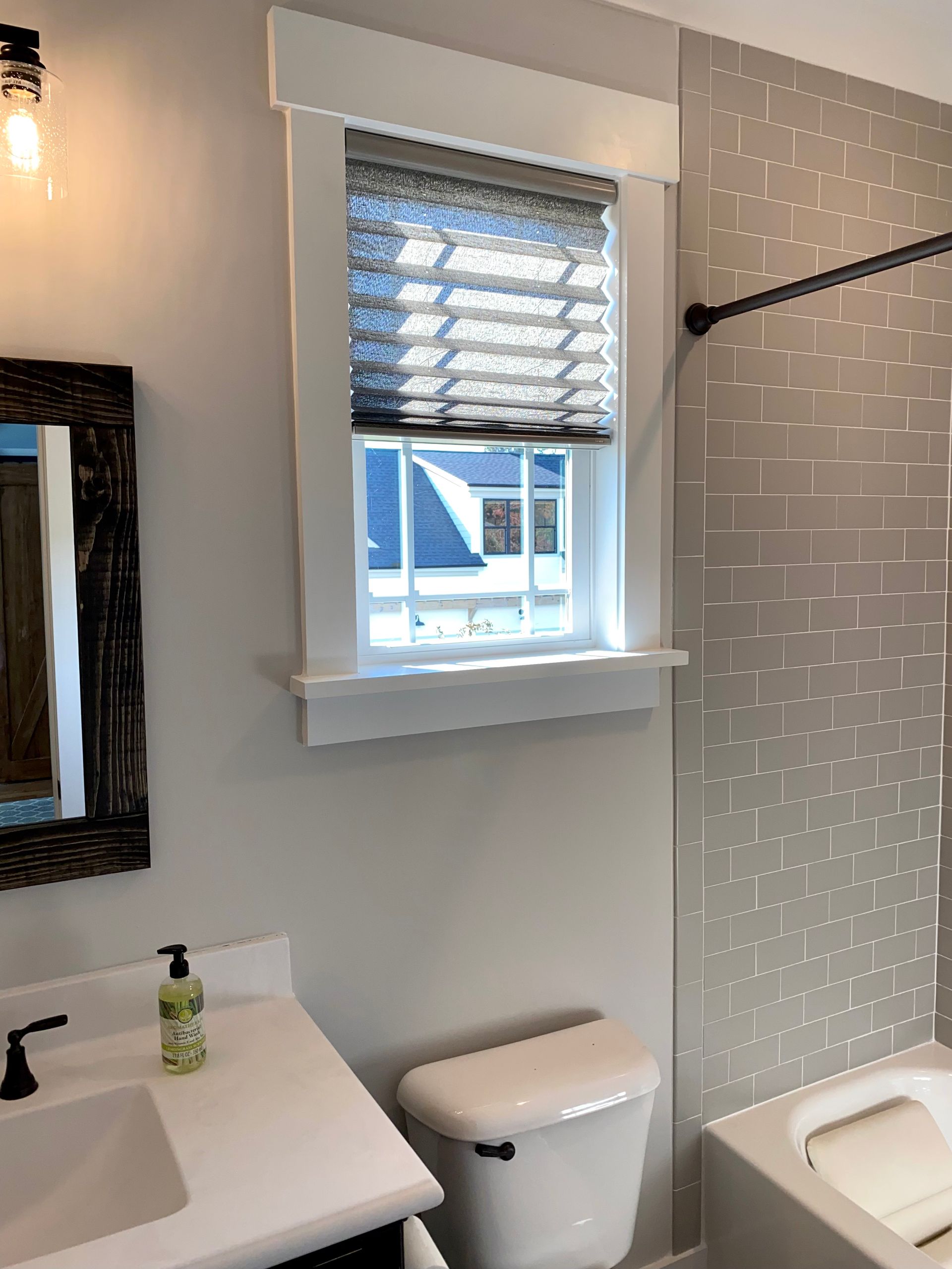 Bathroom with window, toilet, and sink; window has shade and trim. Gray and white color scheme.