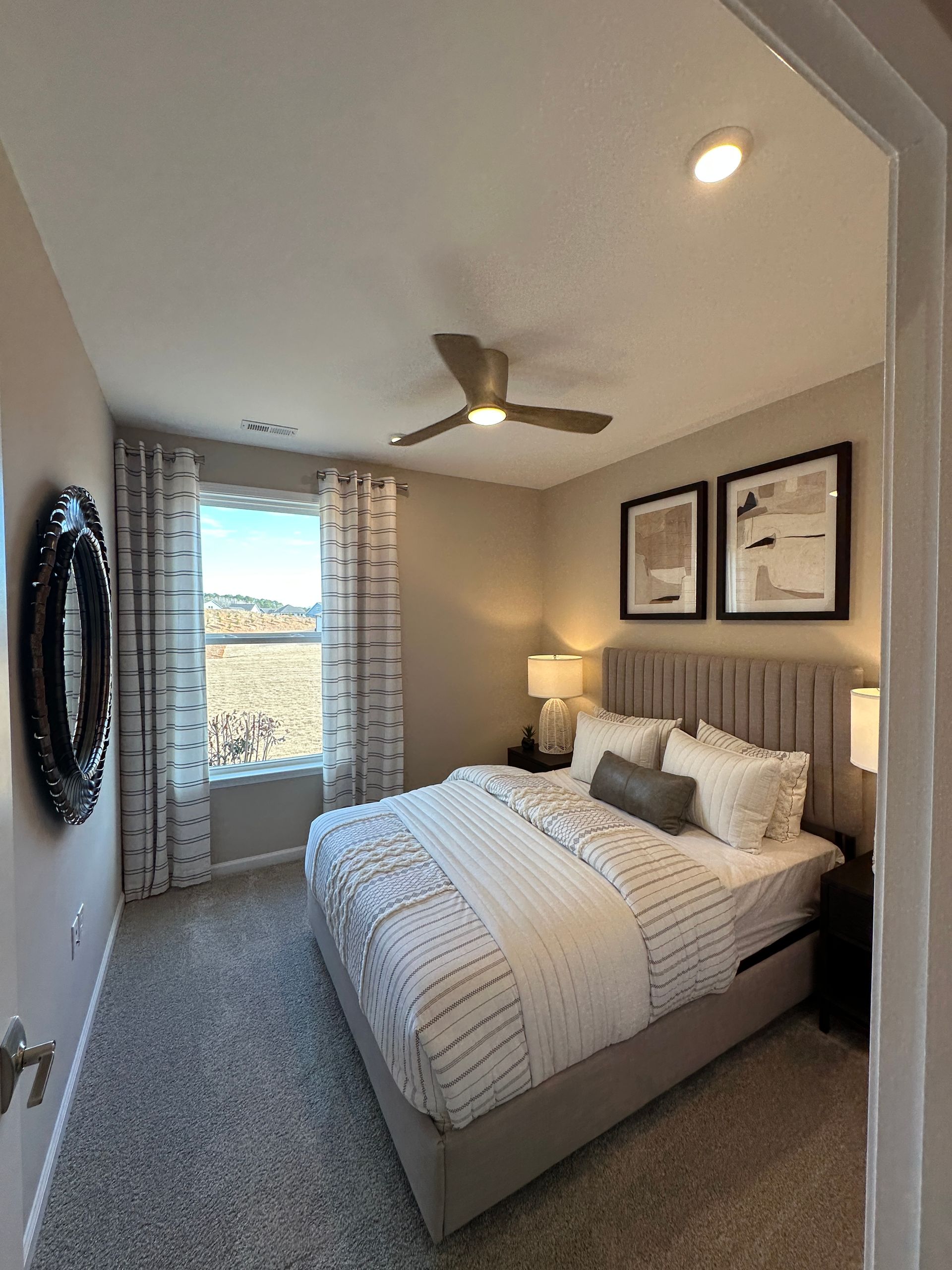 Bedroom with bed, nightstands, window with curtains, and artwork. Grey walls and carpet.