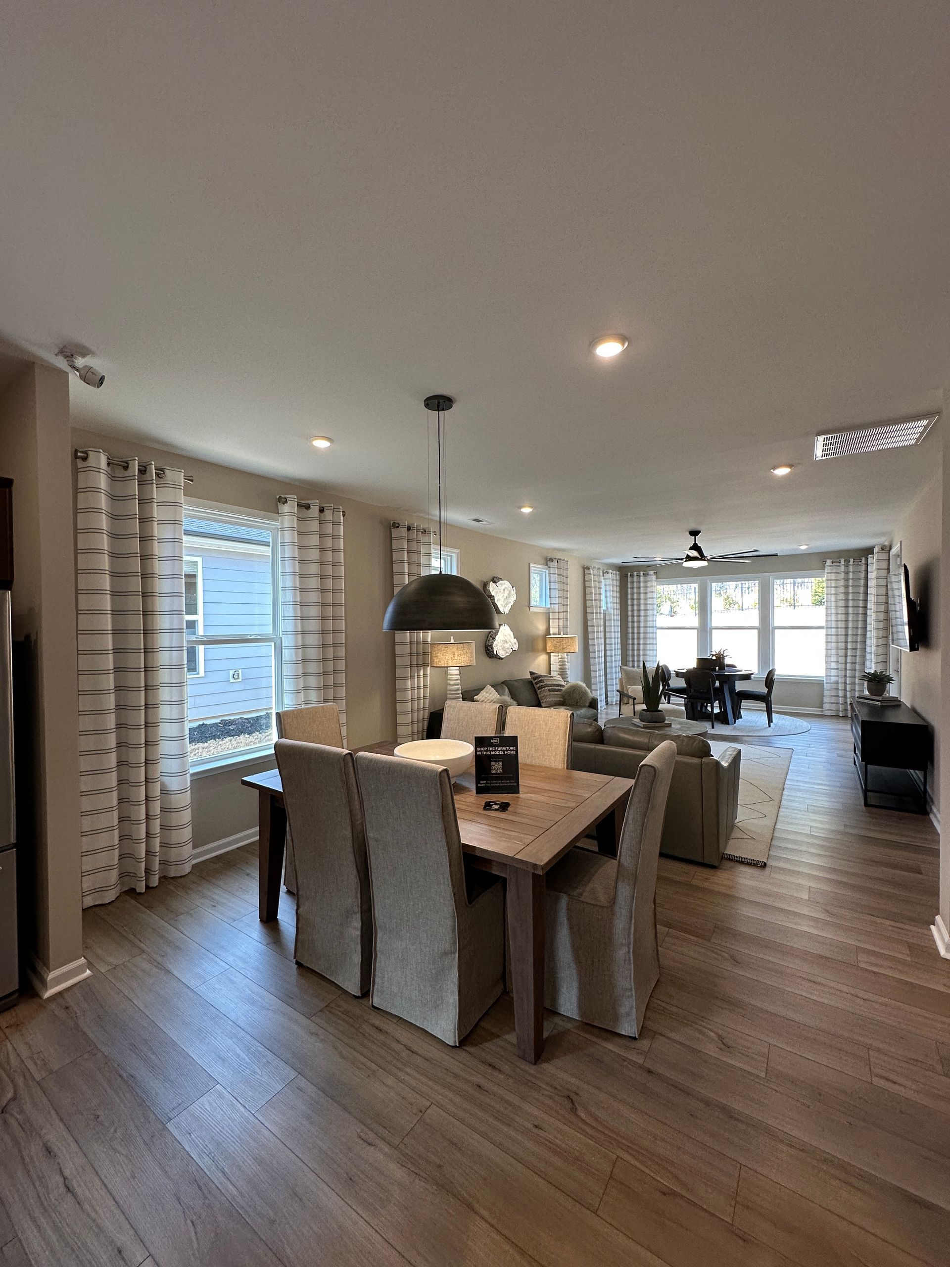Dining area with wooden table and chairs, adjacent to a living room with a couch and large windows.