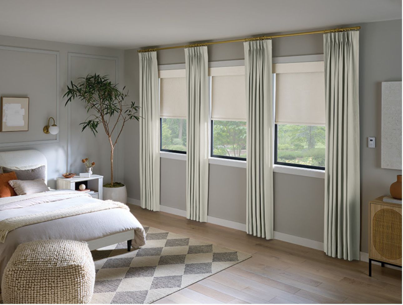 Bedroom with bed, rug, tree, three windows with blinds and curtains. Neutral colors, light and airy.