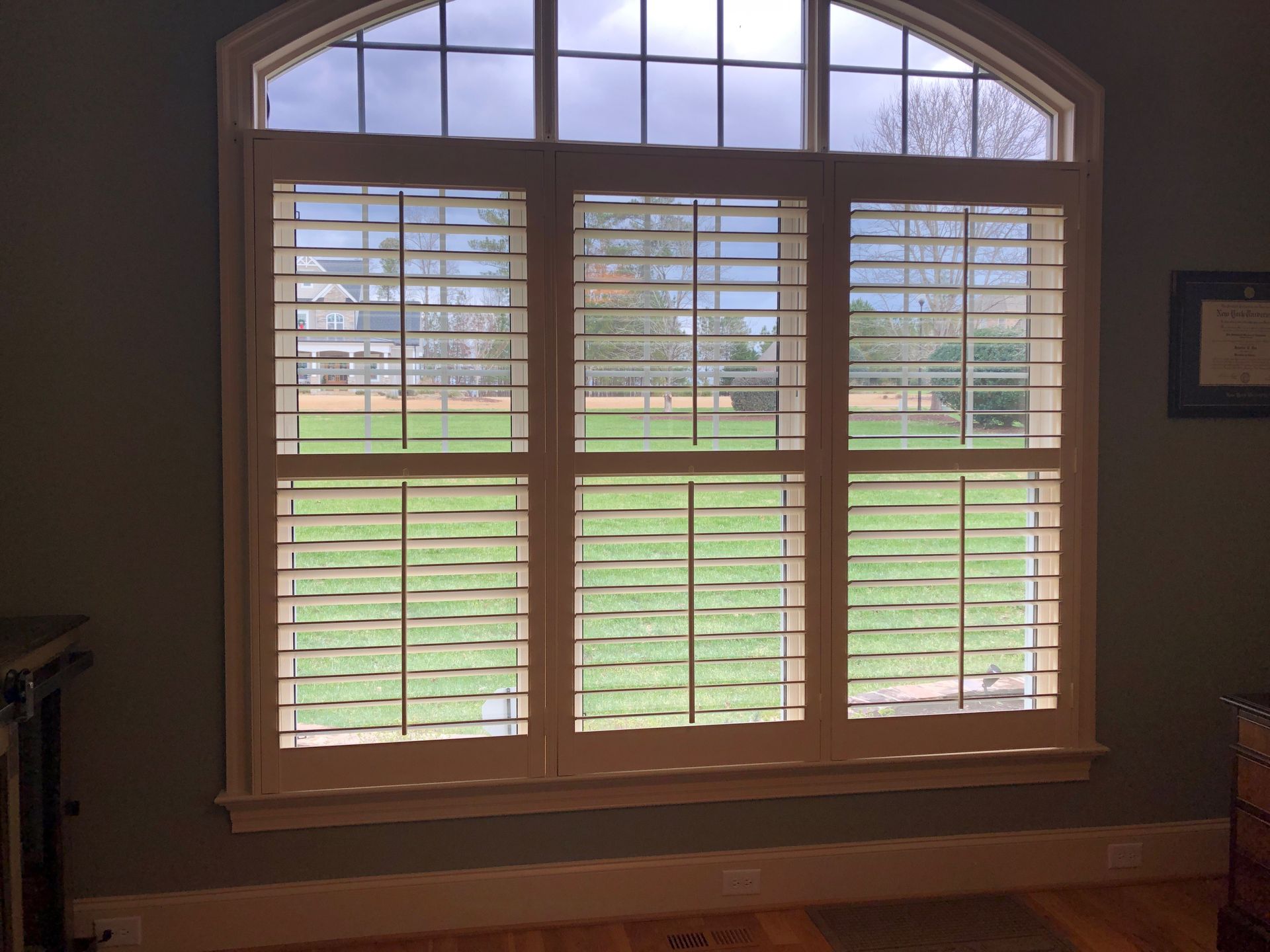 Window with white shutters; view of a green lawn and sky.