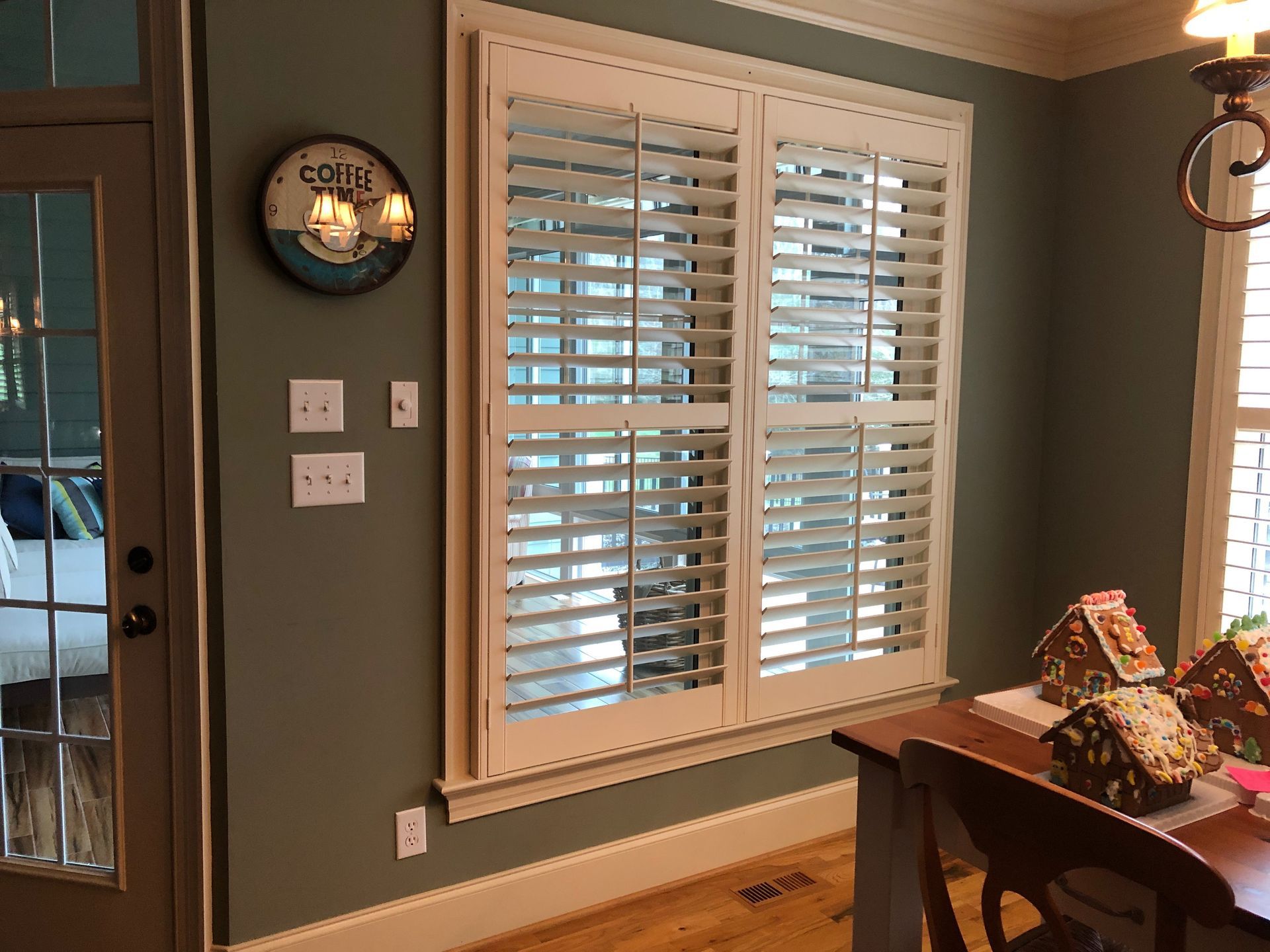 Interior dining area with window shutters and a decorative sign, next to a glass door.