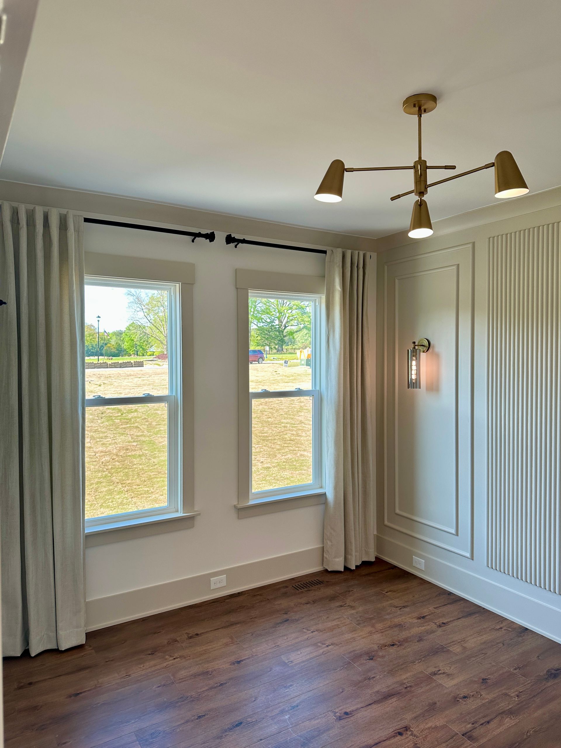 A room with two windows, light curtains, decorative wall paneling, and a modern light fixture.