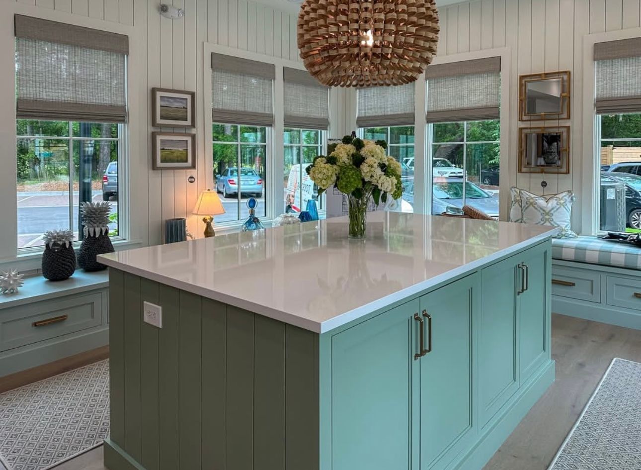 Kitchen with green island, white countertop, windows with shades, and a chandelier.