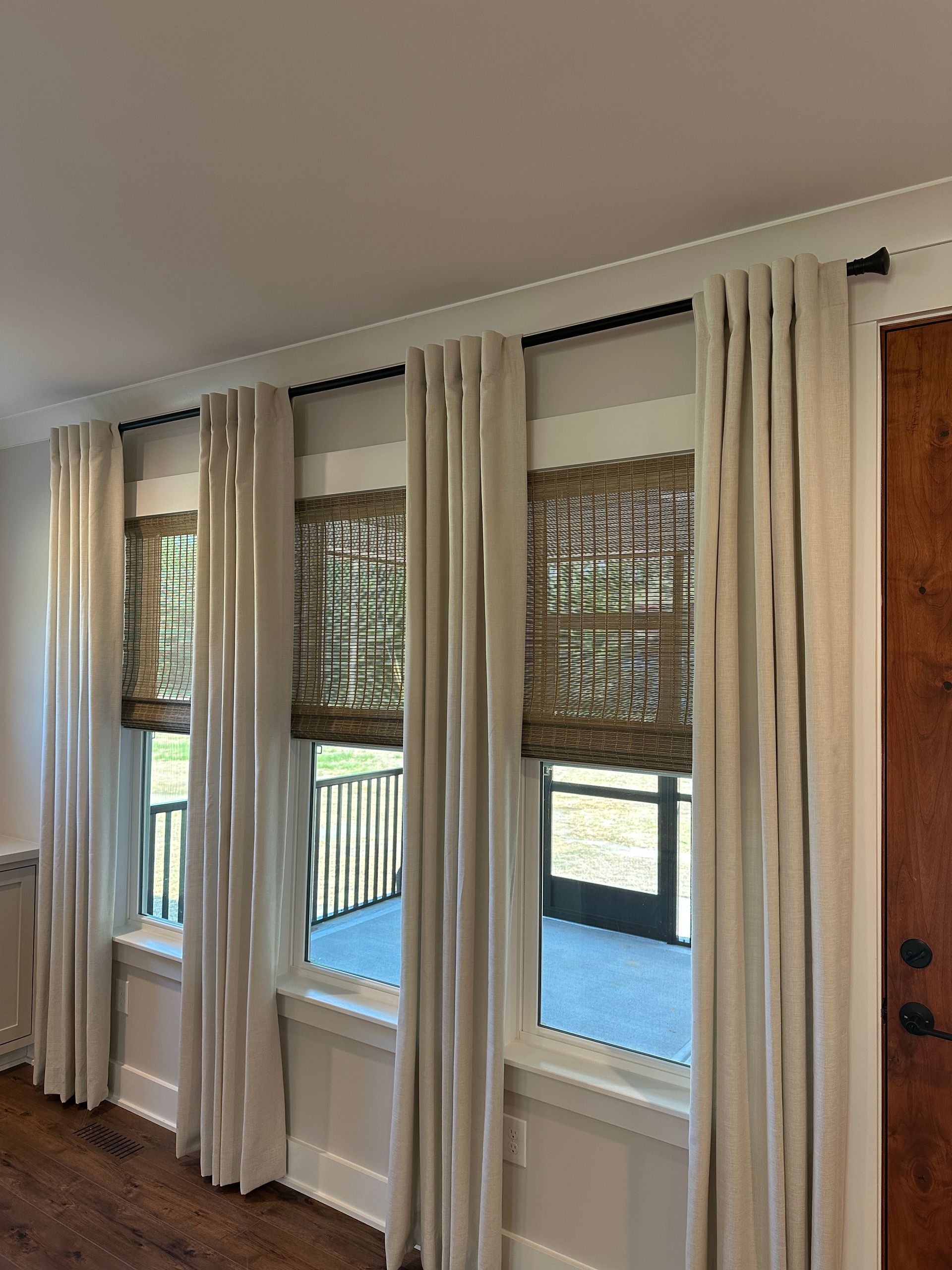 Three windows with woven shades and light curtains, set in a white-trimmed wall.