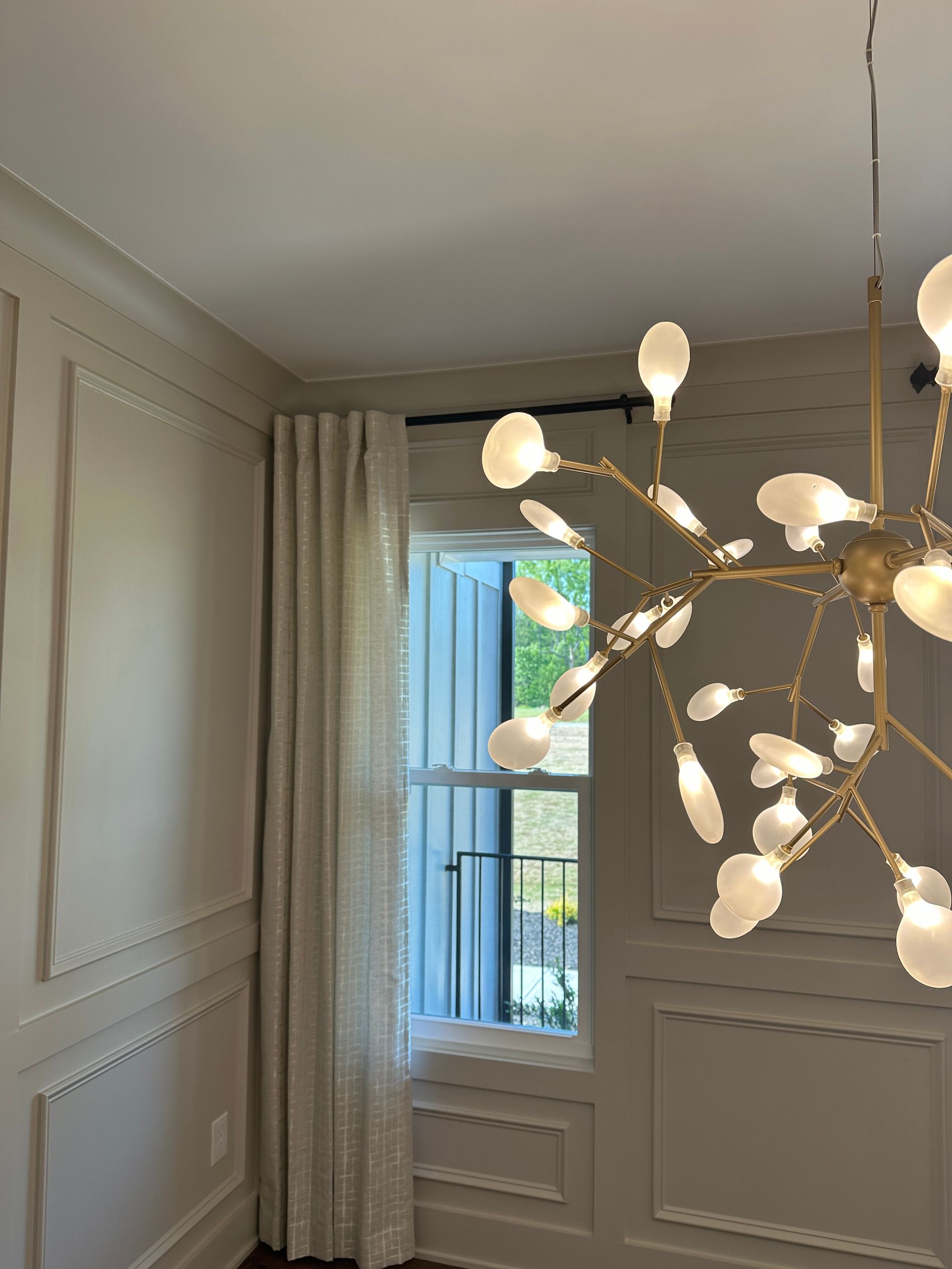 Dining room with window, drapes, and a modern chandelier. Neutral walls and trim.