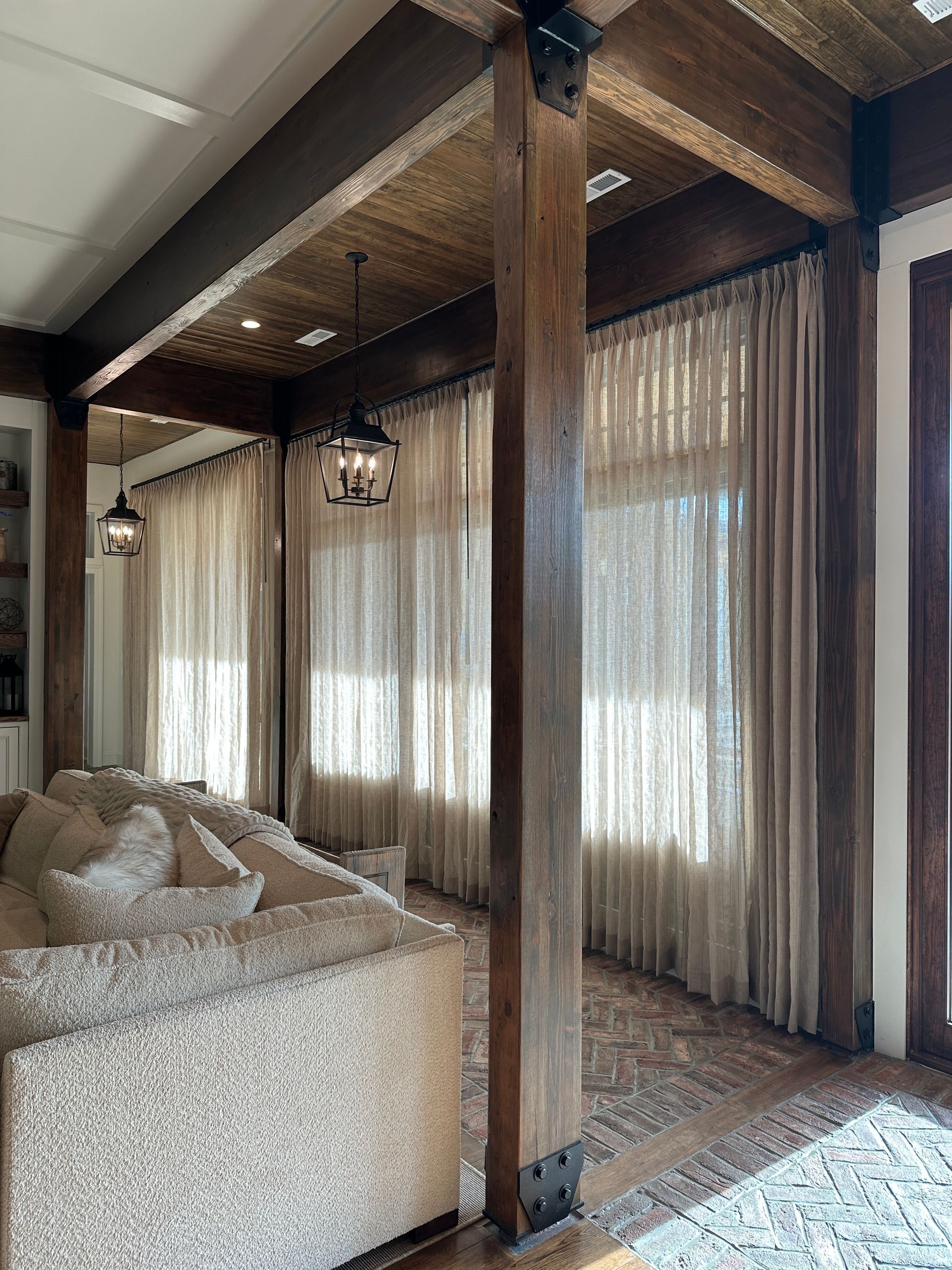 Living room with exposed wood beams, neutral-toned curtains, and a textured sofa.