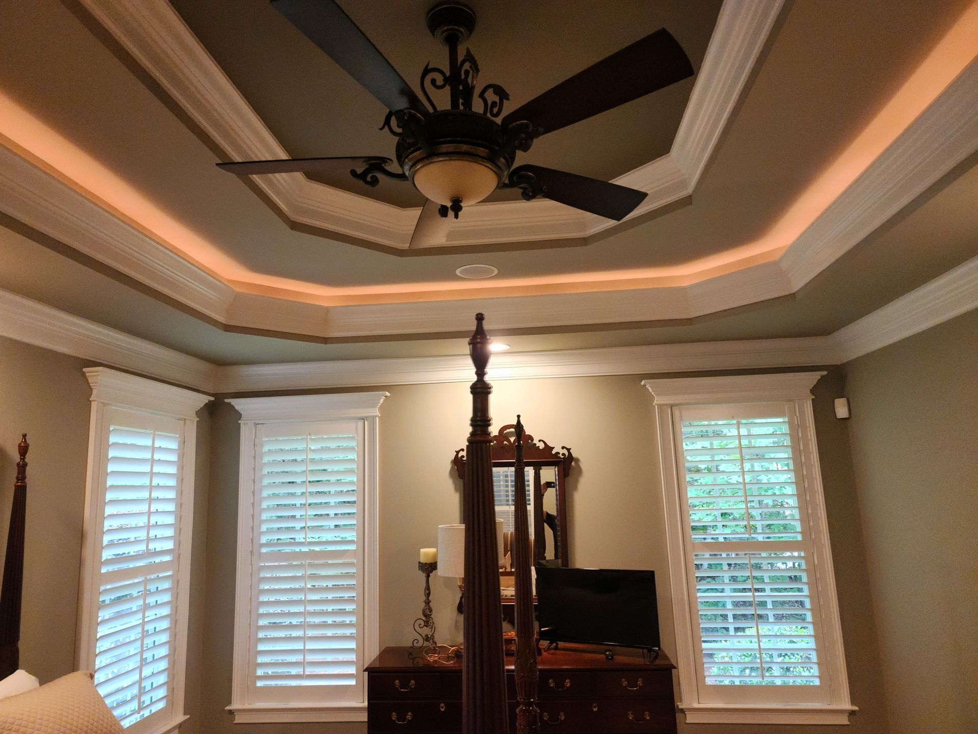 Bedroom ceiling with ornate crown molding and a ceiling fan, windows with shutters, and a dark wooden dresser.