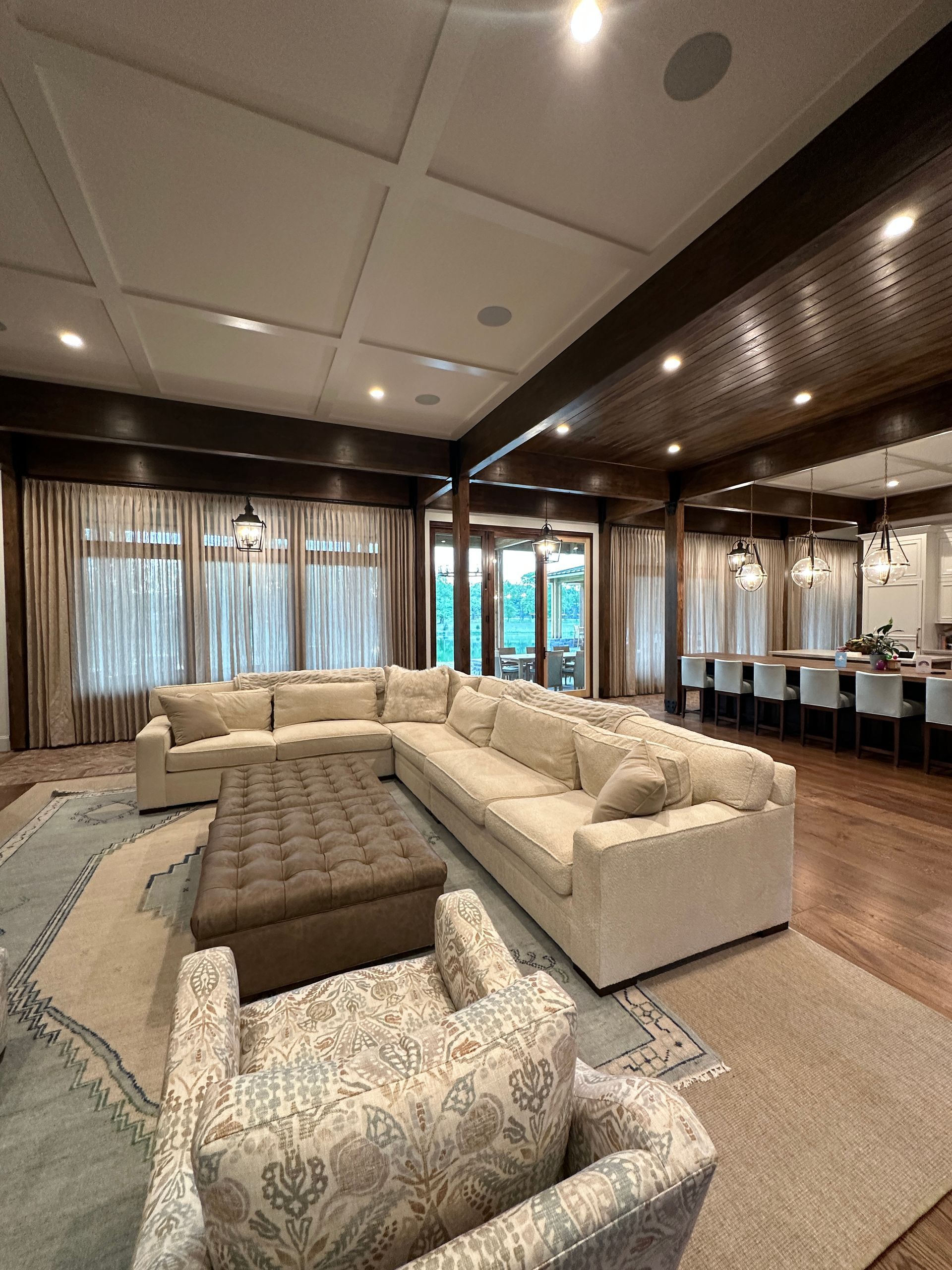 Spacious living room with a cream sectional, patterned rug, wood beams, and large windows.