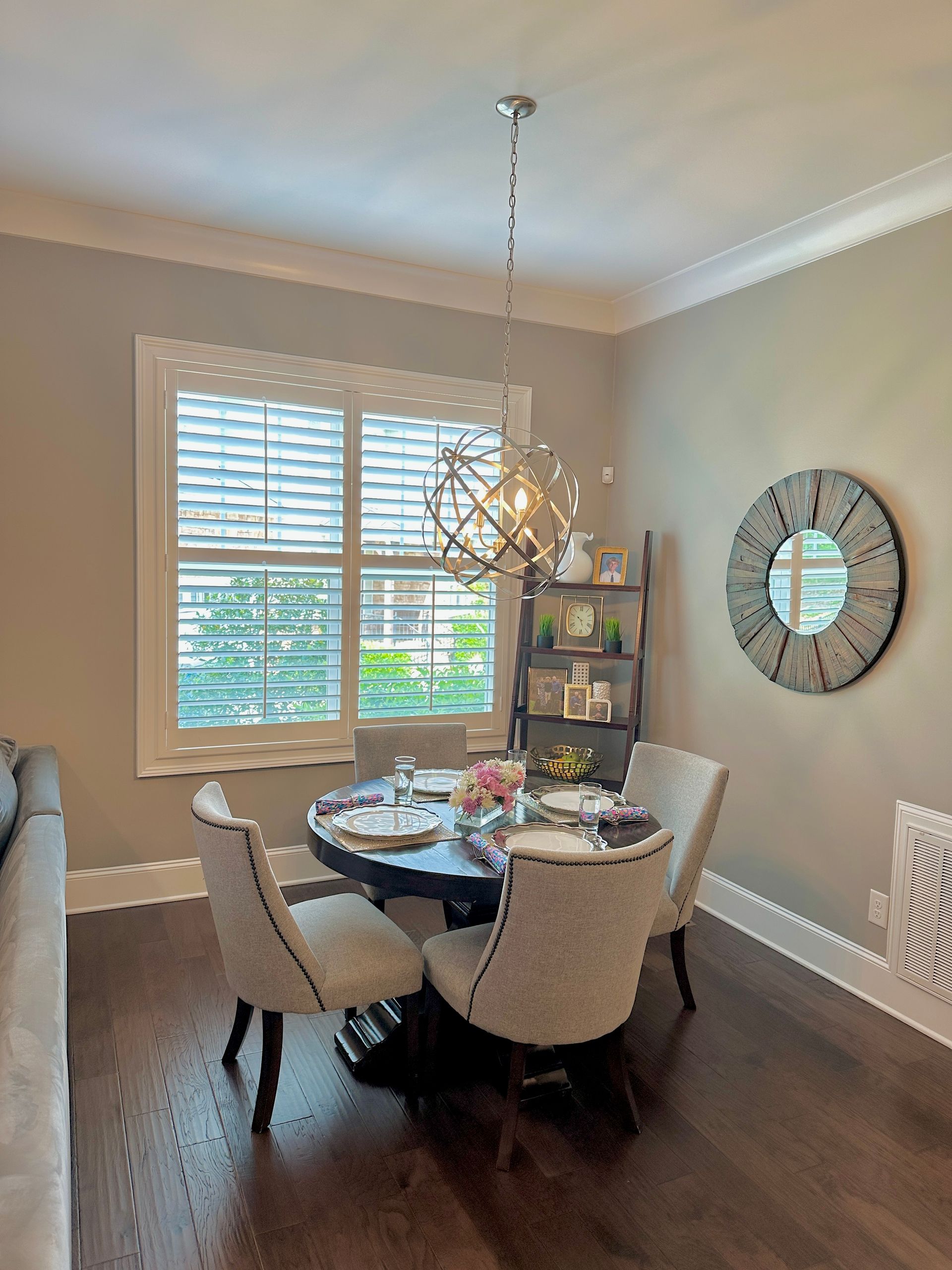 Dining room with round table, chairs, and chandelier; window with blinds.