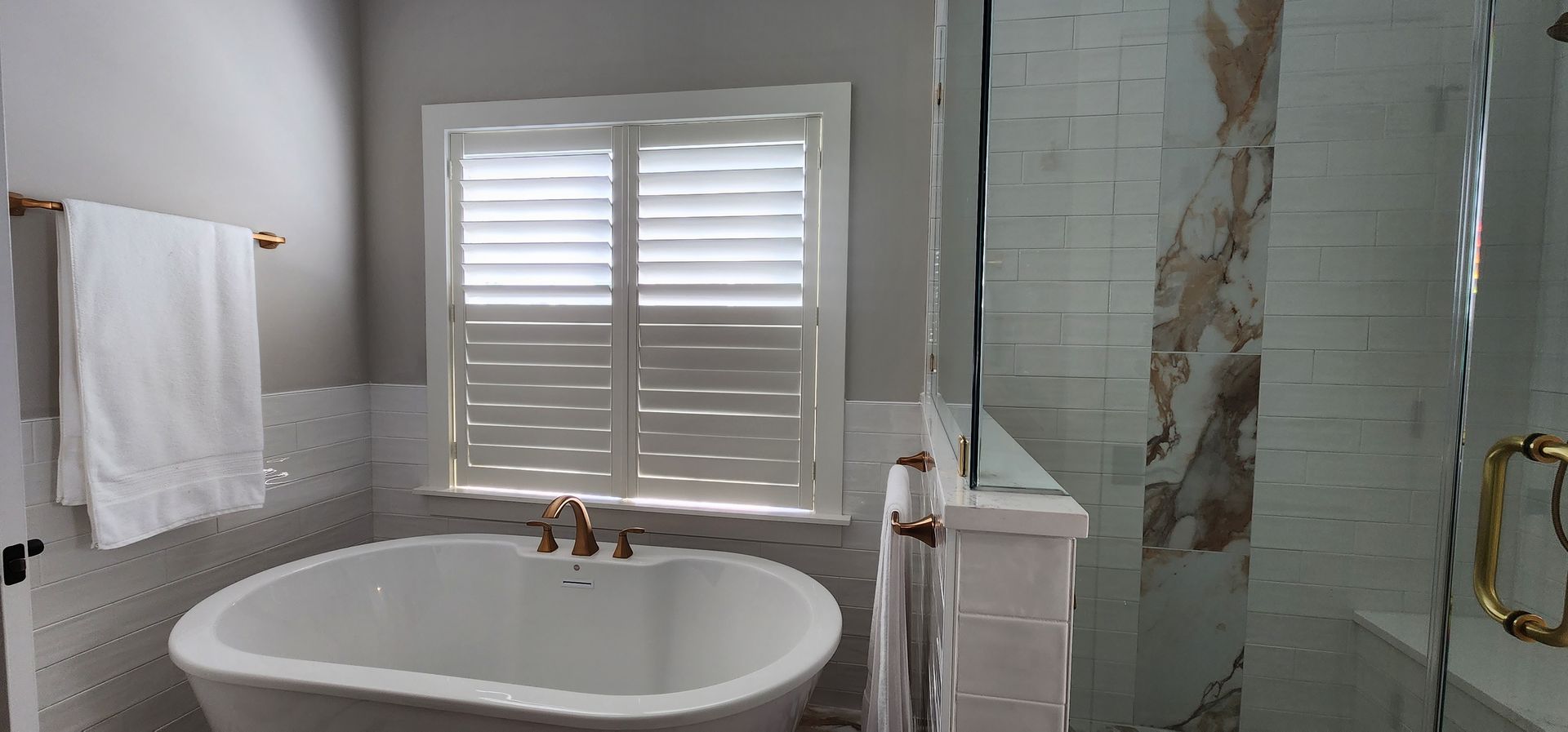 Bathroom with a white bathtub, shutters, and a glass shower.