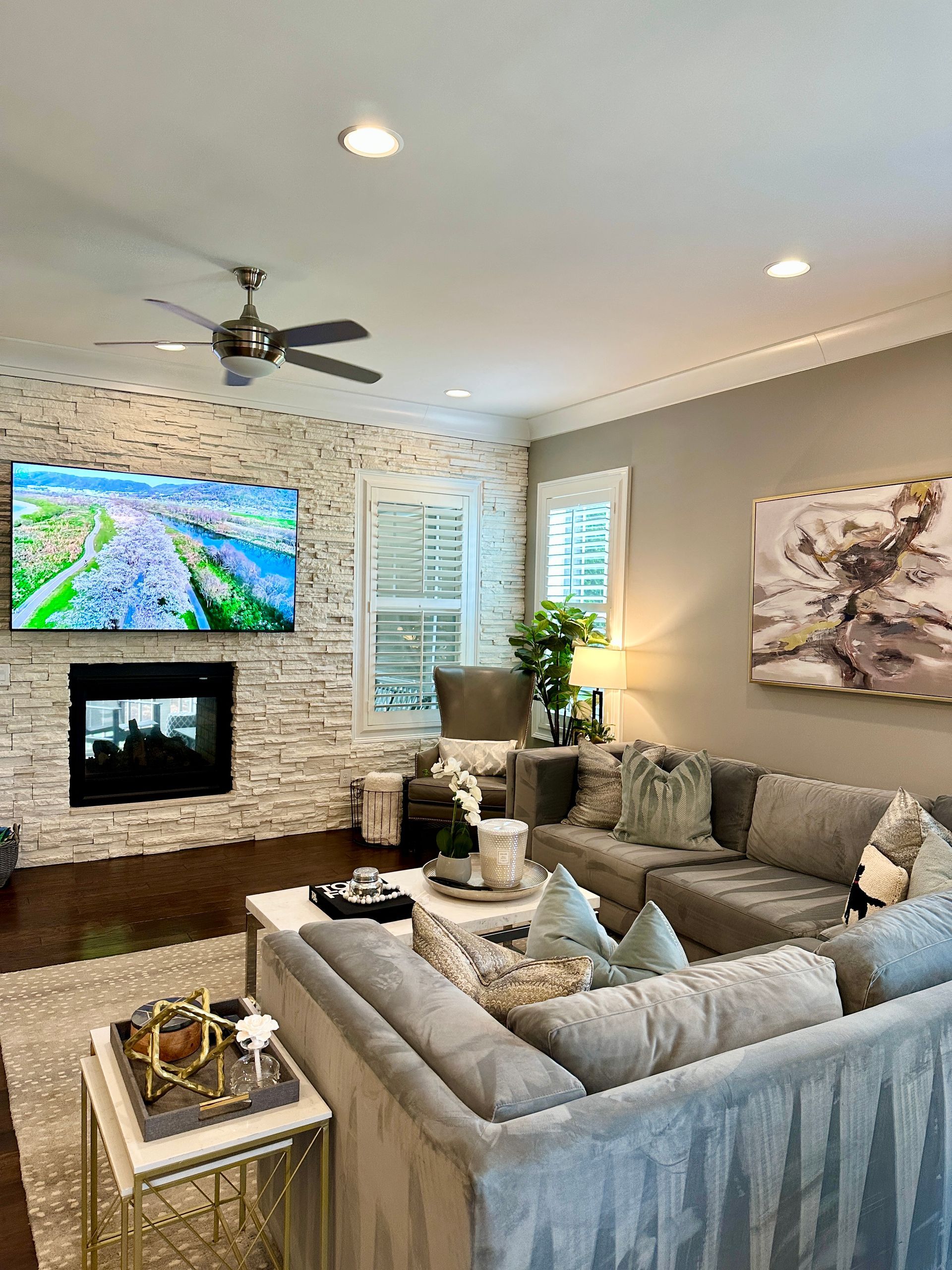 Living room with gray sectional sofa, fireplace with TV, and decorative art.