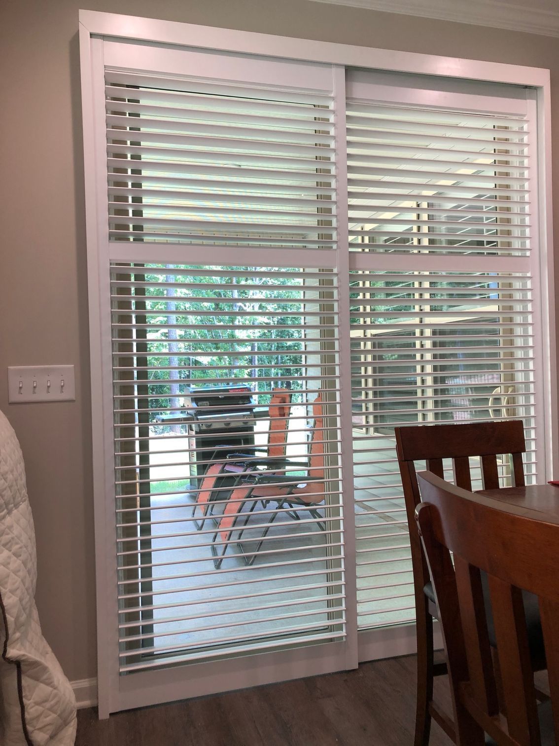 White shuttered sliding glass door, leading to a patio with chairs and a grill.