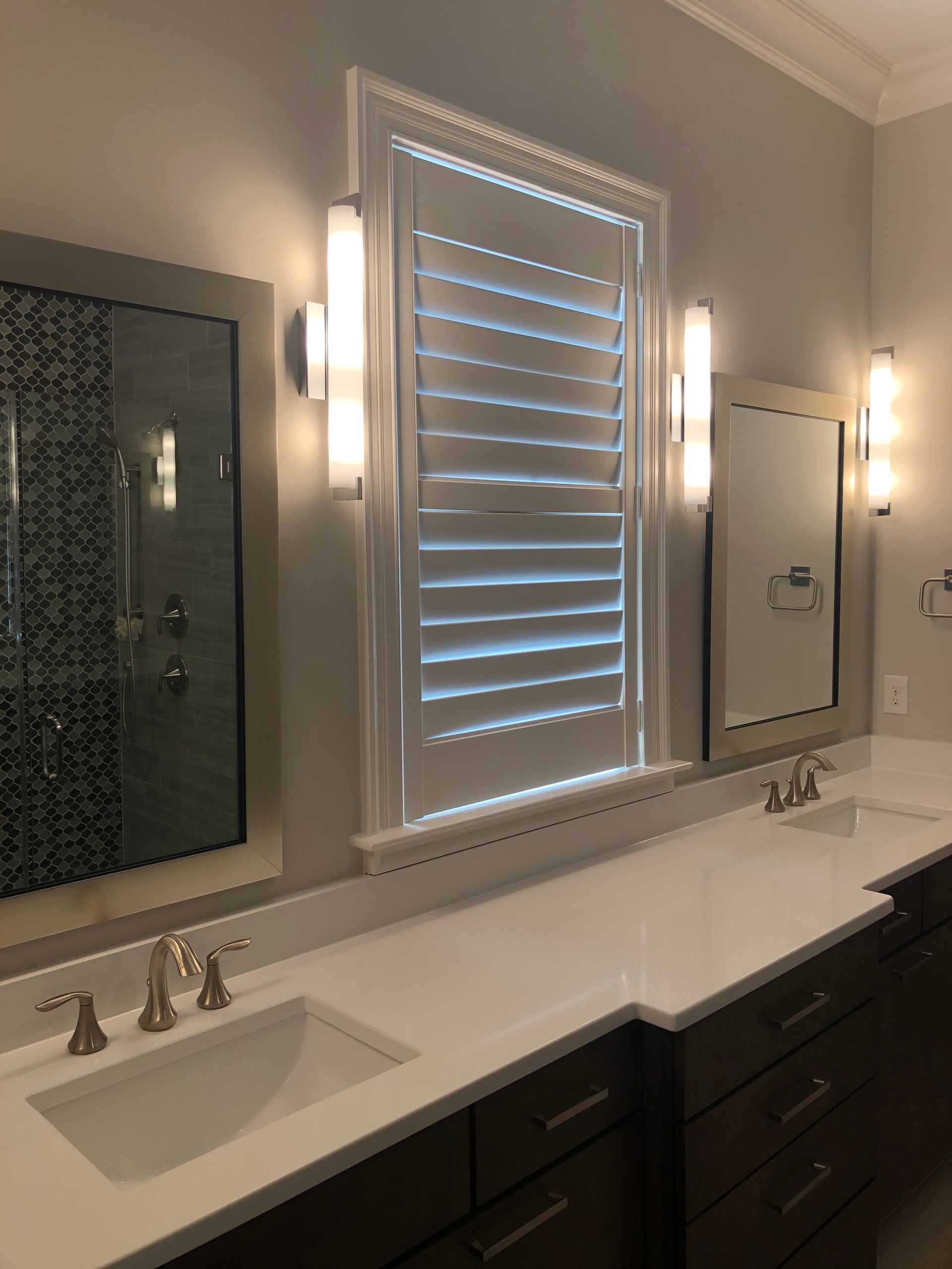 Bathroom vanity with two sinks, mirrors, and a shuttered window.