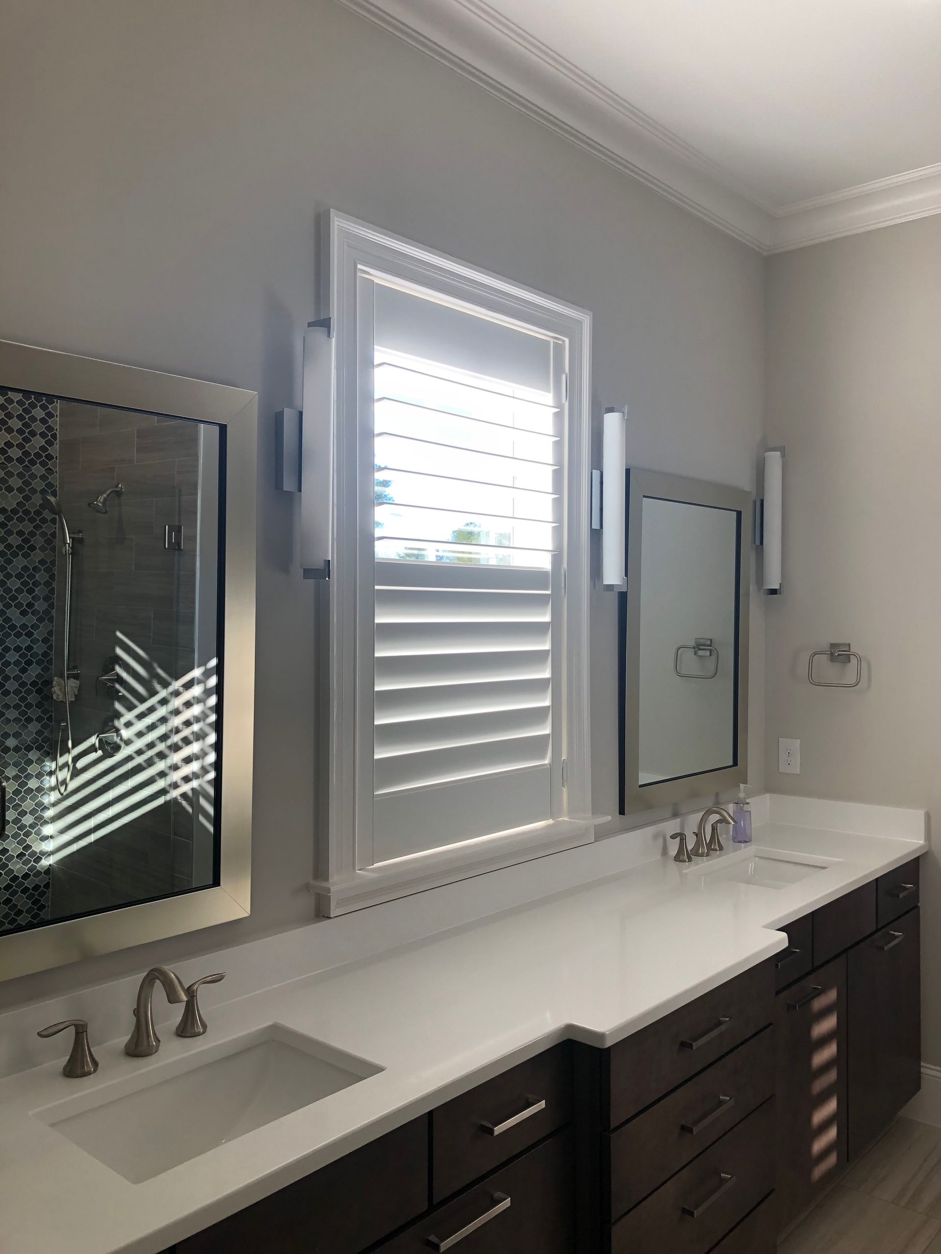 Bathroom with white countertops, dark cabinets, mirrors, and a shuttered window.