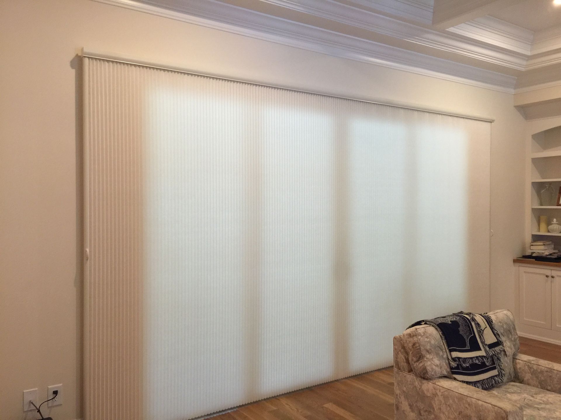 Vertical blinds covering a large window; white walls, ceiling details, and a chair are visible.