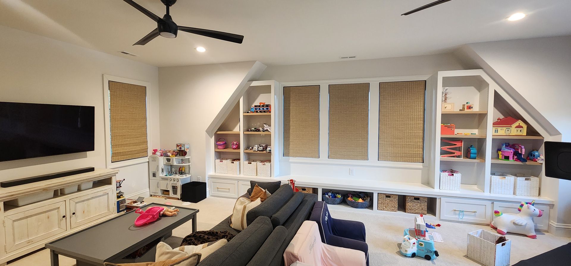 Spacious playroom with built-in storage, a sectional sofa, and a ceiling fan.