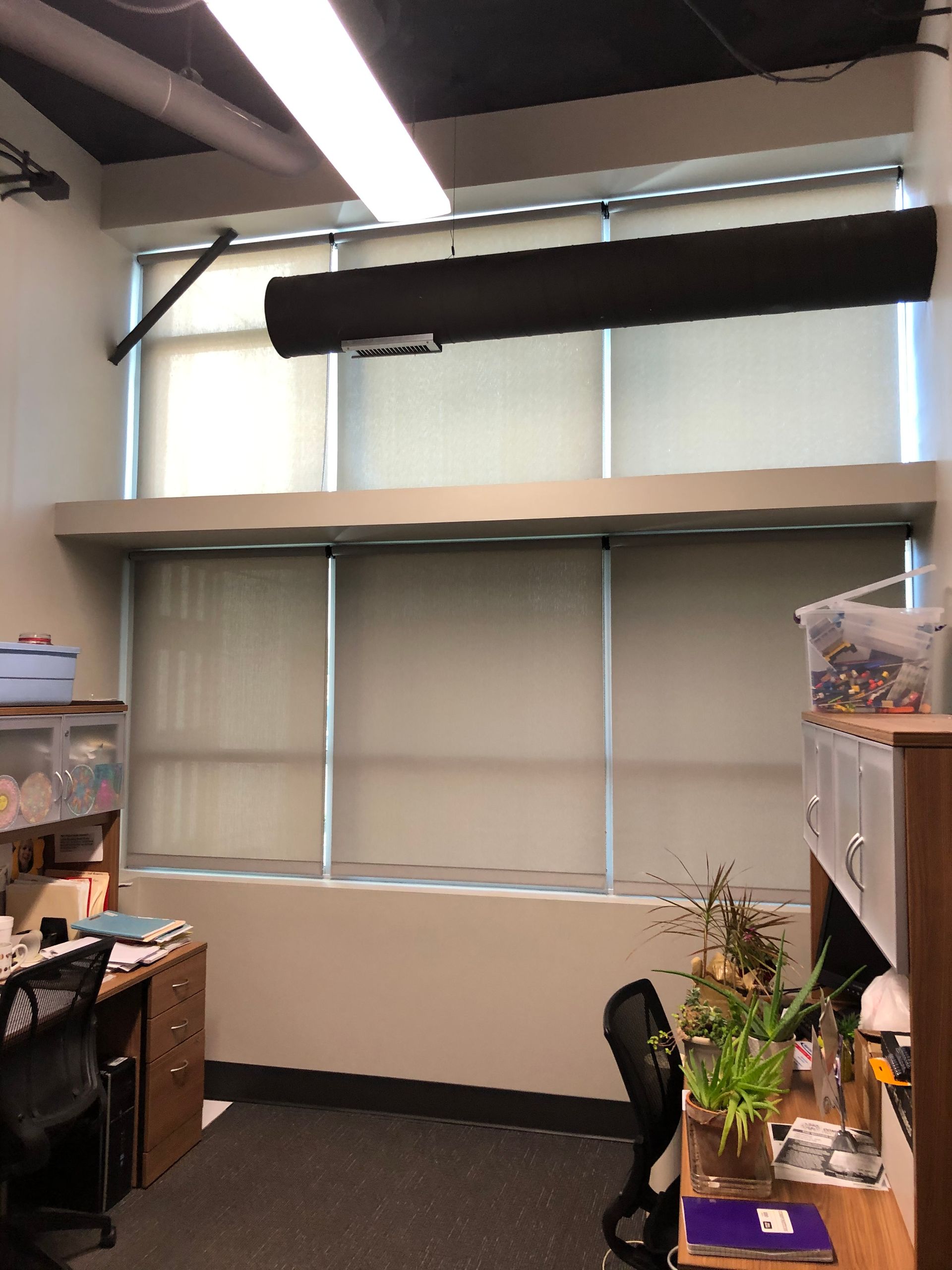 Office interior with windows, desks, and shades. Black sound bar above the upper windows.