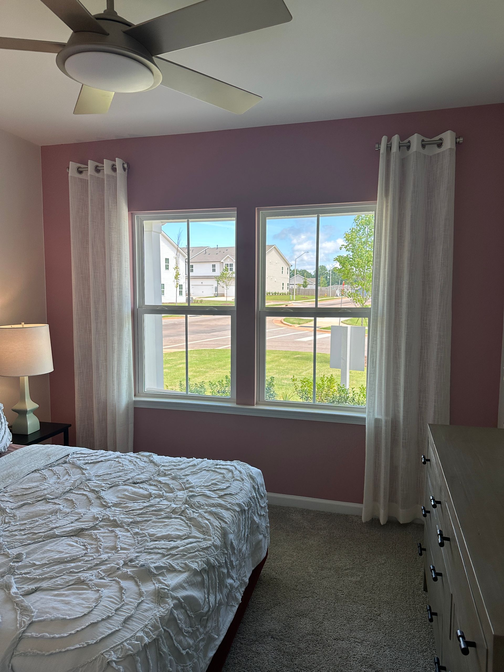 Bedroom with pink walls, two windows, white curtains, and a bed with a white comforter.