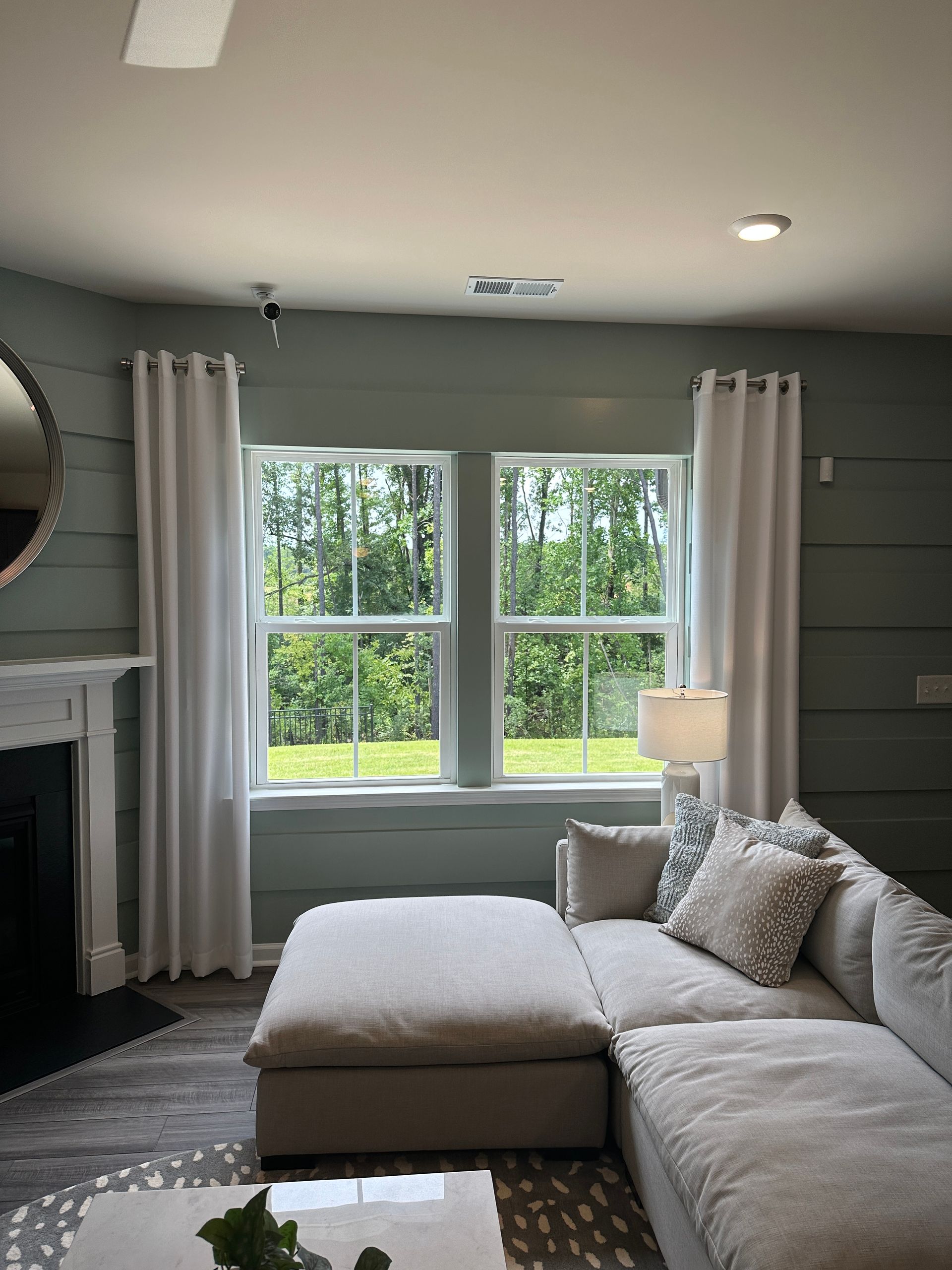 Living room with sage green paneled walls, two windows, and a gray sectional sofa.