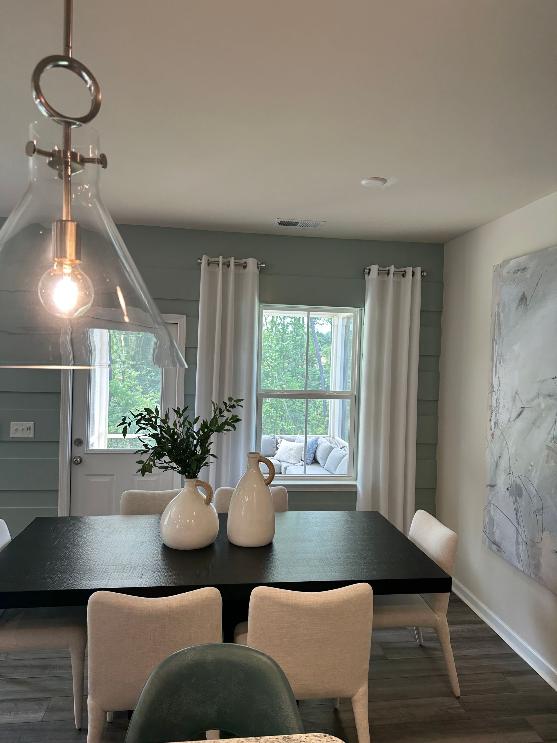 Dining room with black table, white chairs, light blue walls, and large abstract art.