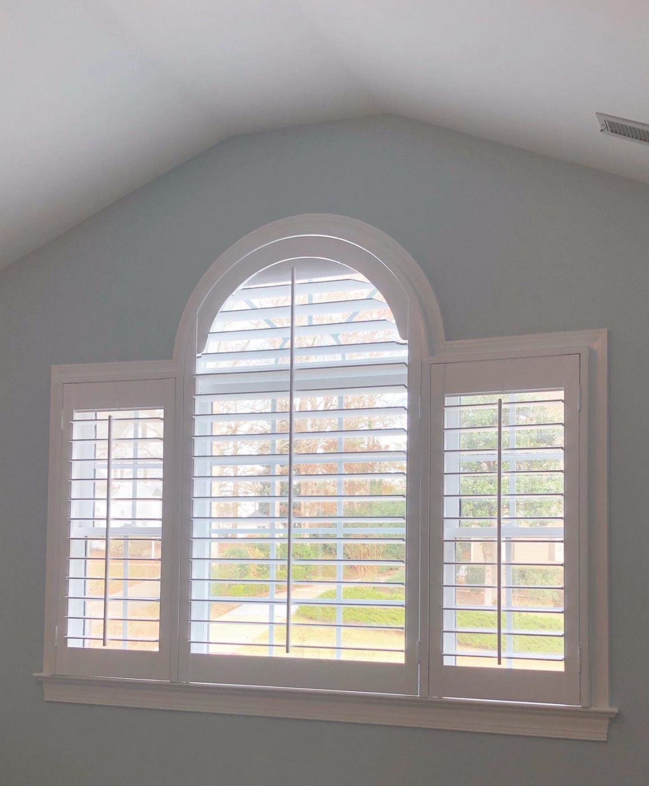 White shuttered window, arched top, set in a light blue wall.