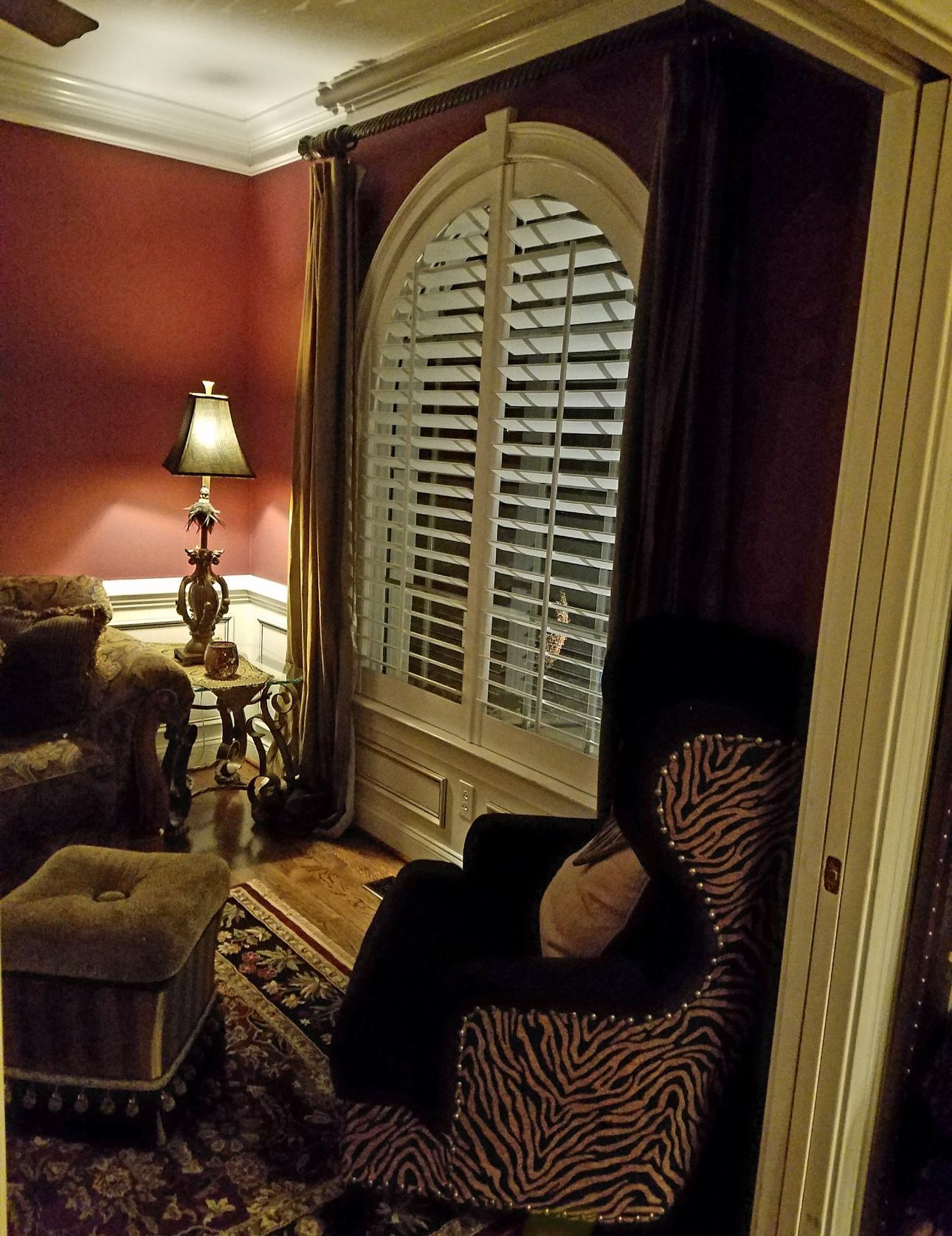 Red-walled room with a zebra-print chair, arched window with shutters, and a lamp.