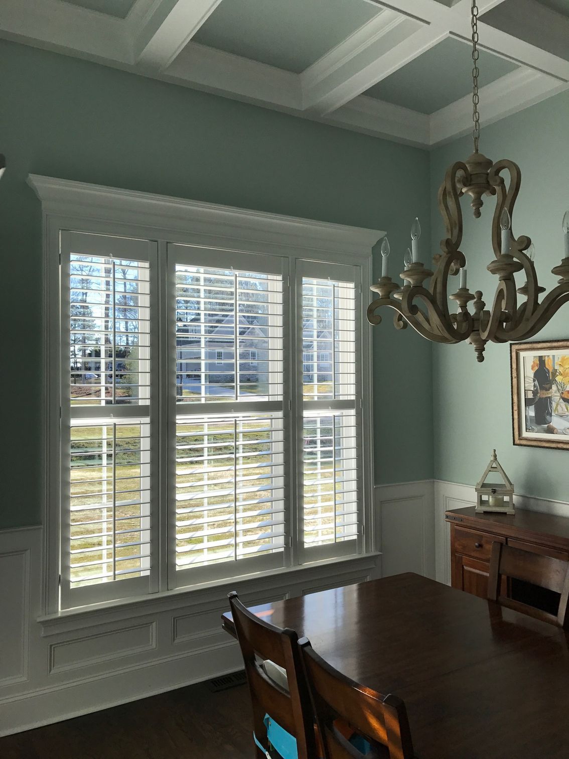Dining room with shutters, chandelier, and a table. Blue-green walls, white trim, and a dark wood table.