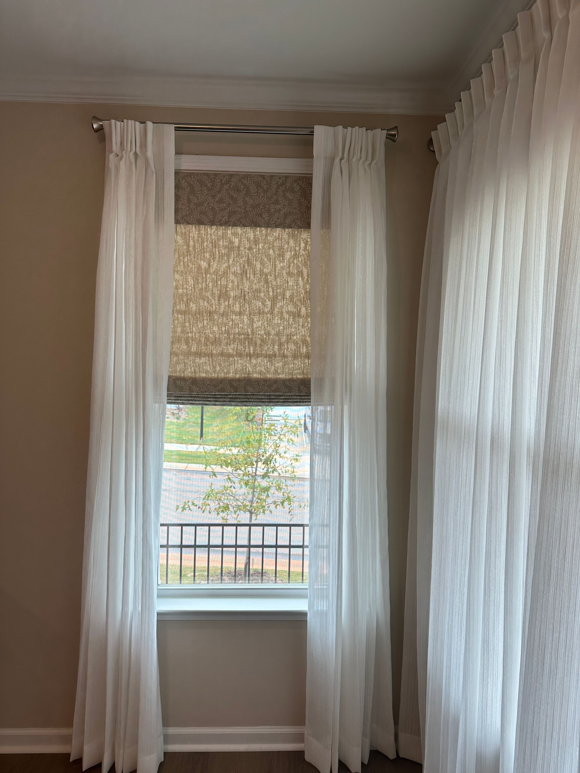 Window with white sheer curtains and a textured shade, in a room with light-colored walls.