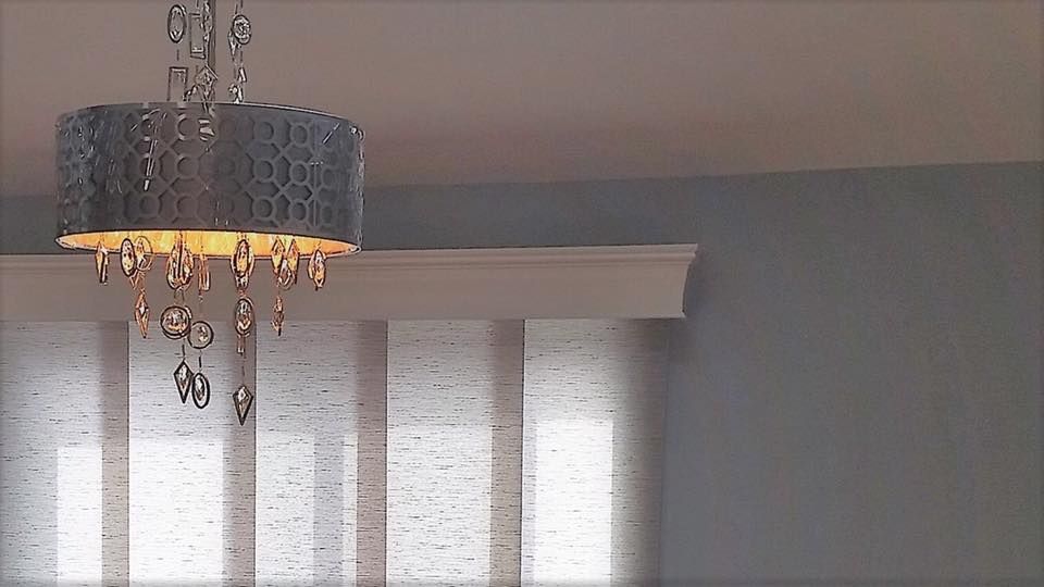 Chandelier hanging above blinds in a room with light blue walls.