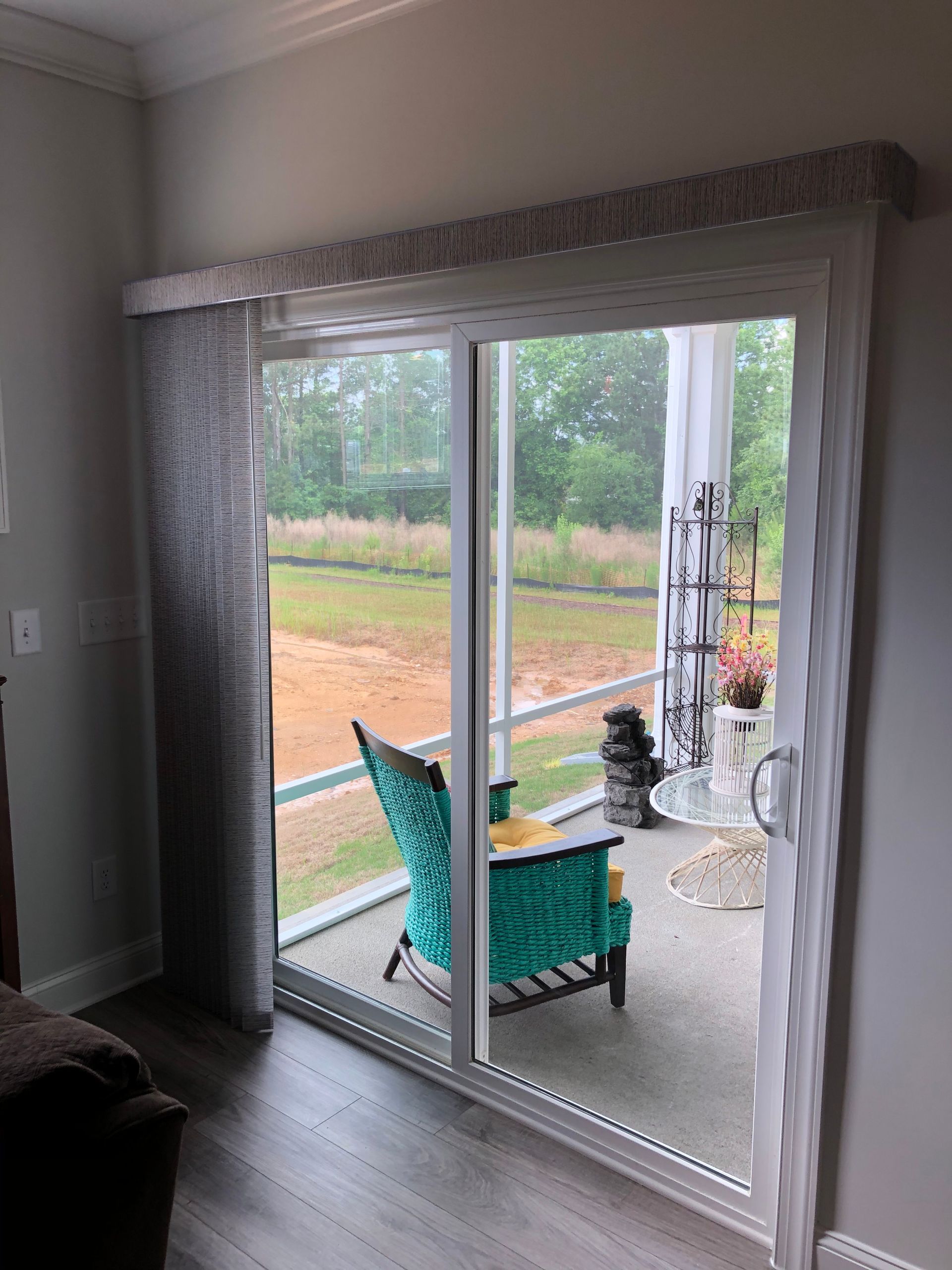 Sliding glass door with sheer vertical blinds. A turquoise chair on a screened patio.