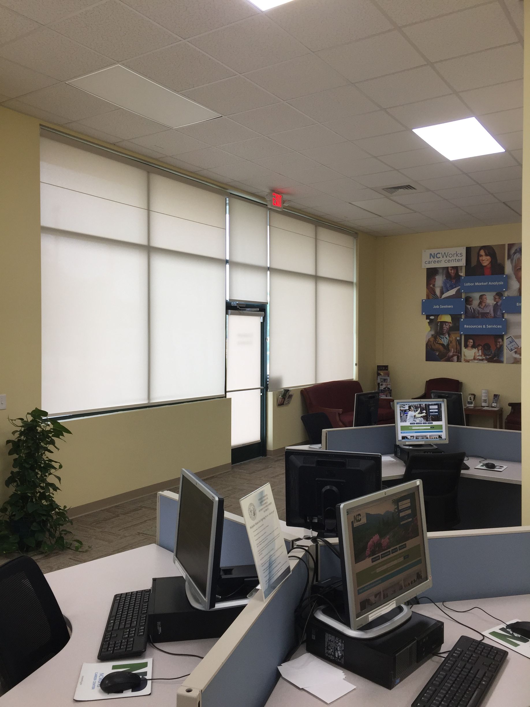 Computer lab with several computers, a door, and window shades.