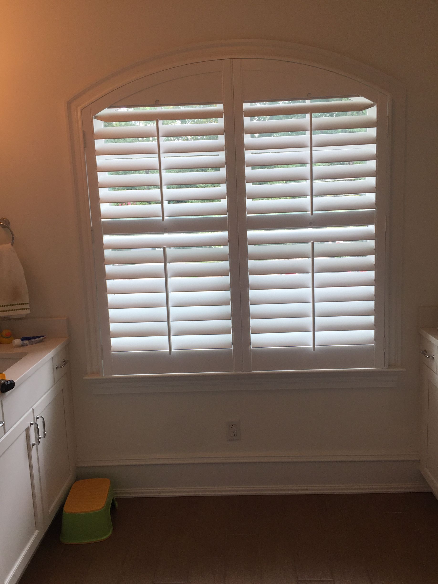 White window shutters in an arched window, with white trim and a brown floor.