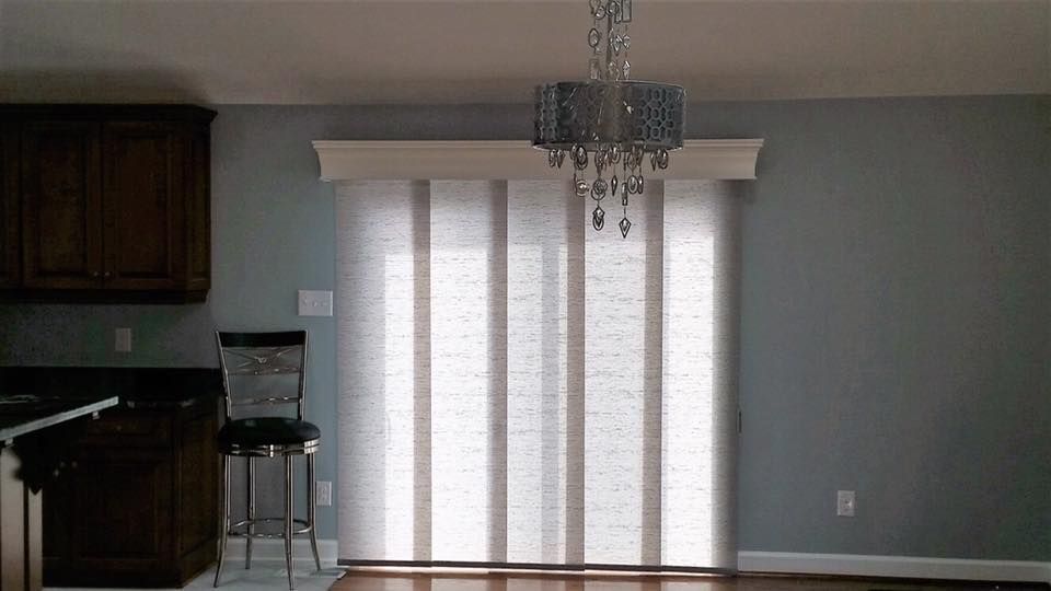 Dining room with vertical blinds, chandelier, and a chair. Light blue walls and dark brown cabinets.