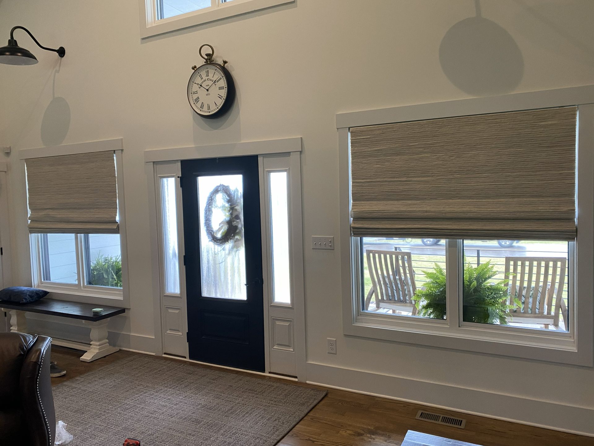 Entryway with a navy door, clock, windows with shades, and outdoor seating visible.
