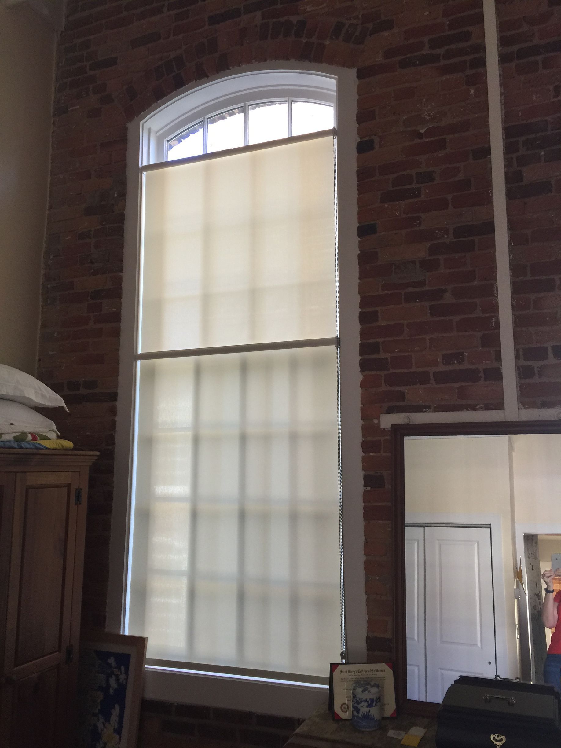 Tall window with arched top, beige shades, against a red brick wall.