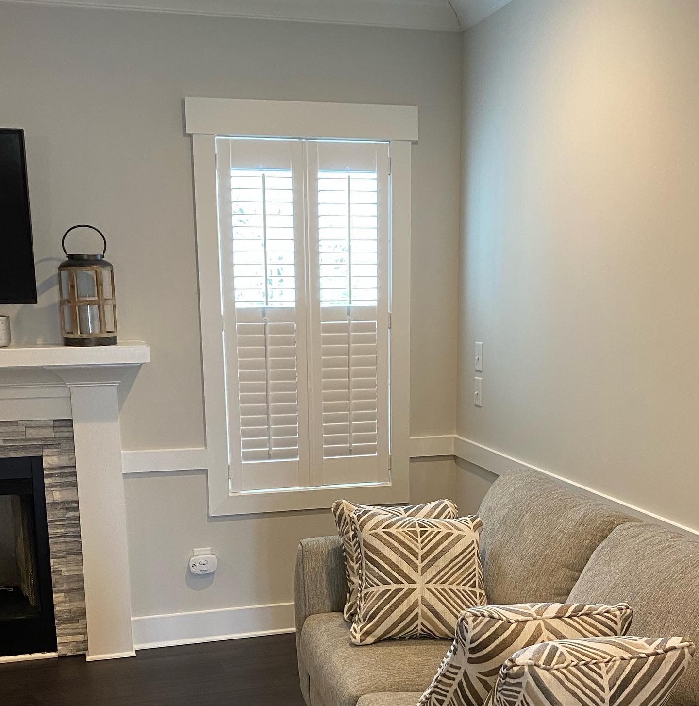 Living room corner with a window, white shutters, a gray sofa, and a fireplace.
