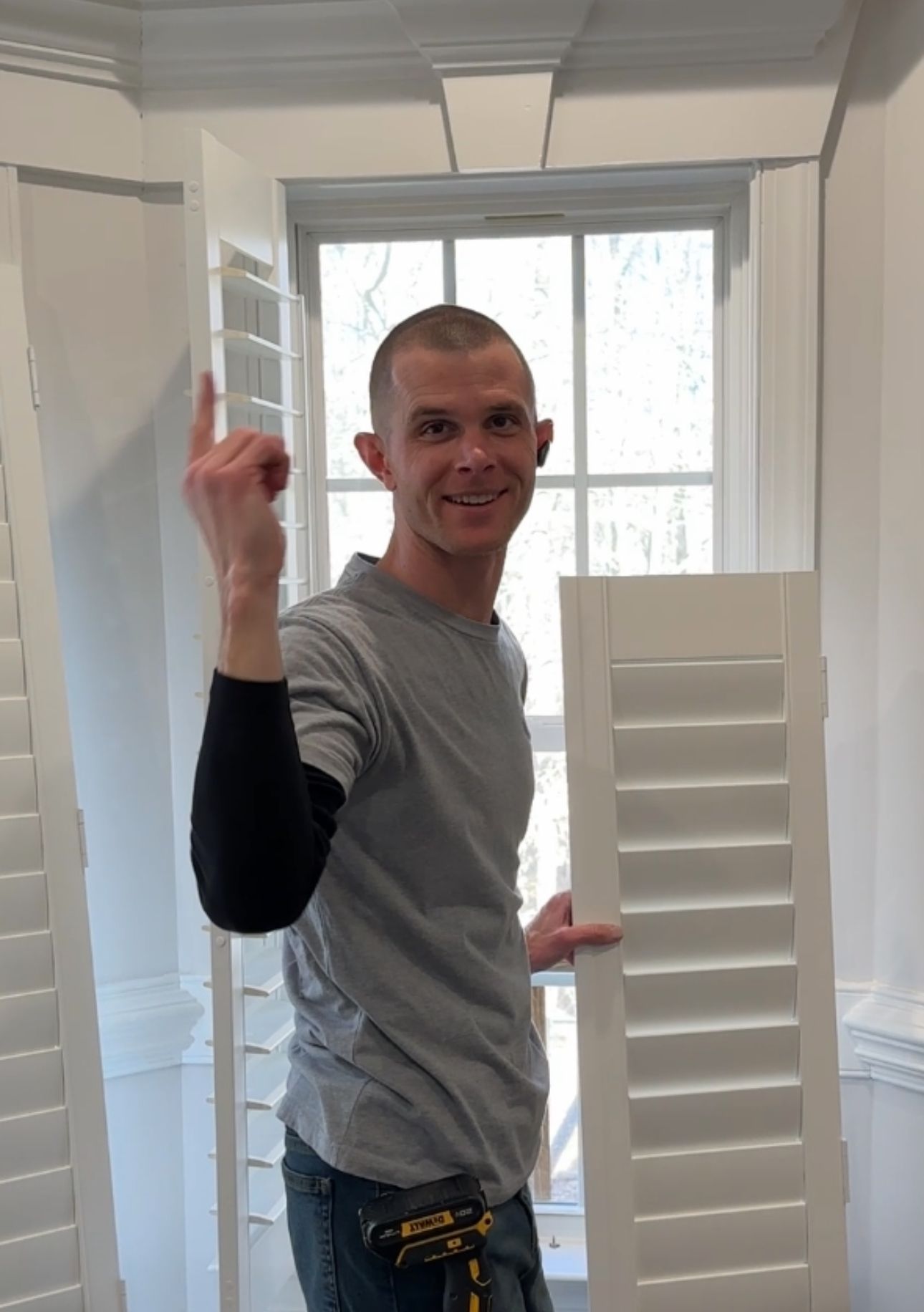 Man holding a white shutter, pointing up. Inside, next to a window.